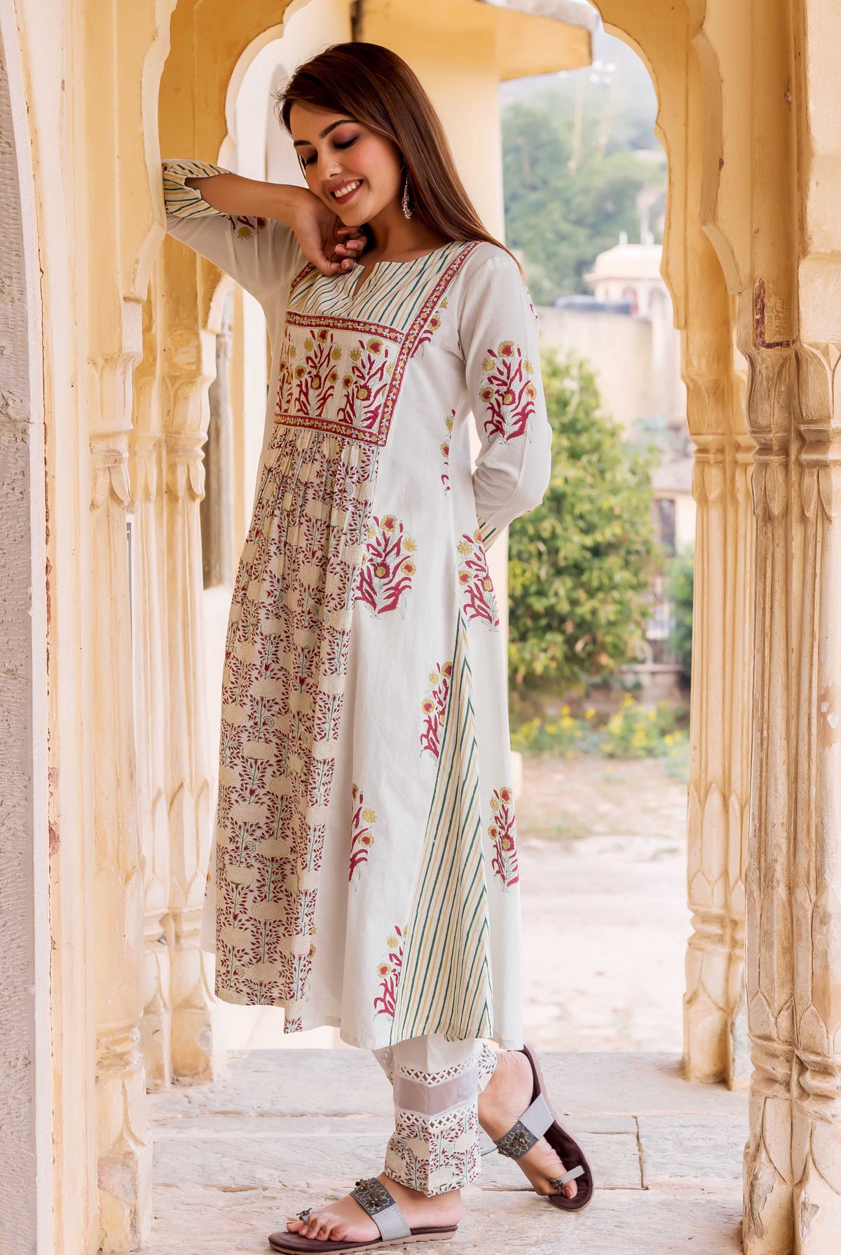 Smiling model in off-white hand block printed kurta with red floral and green striped patterns.