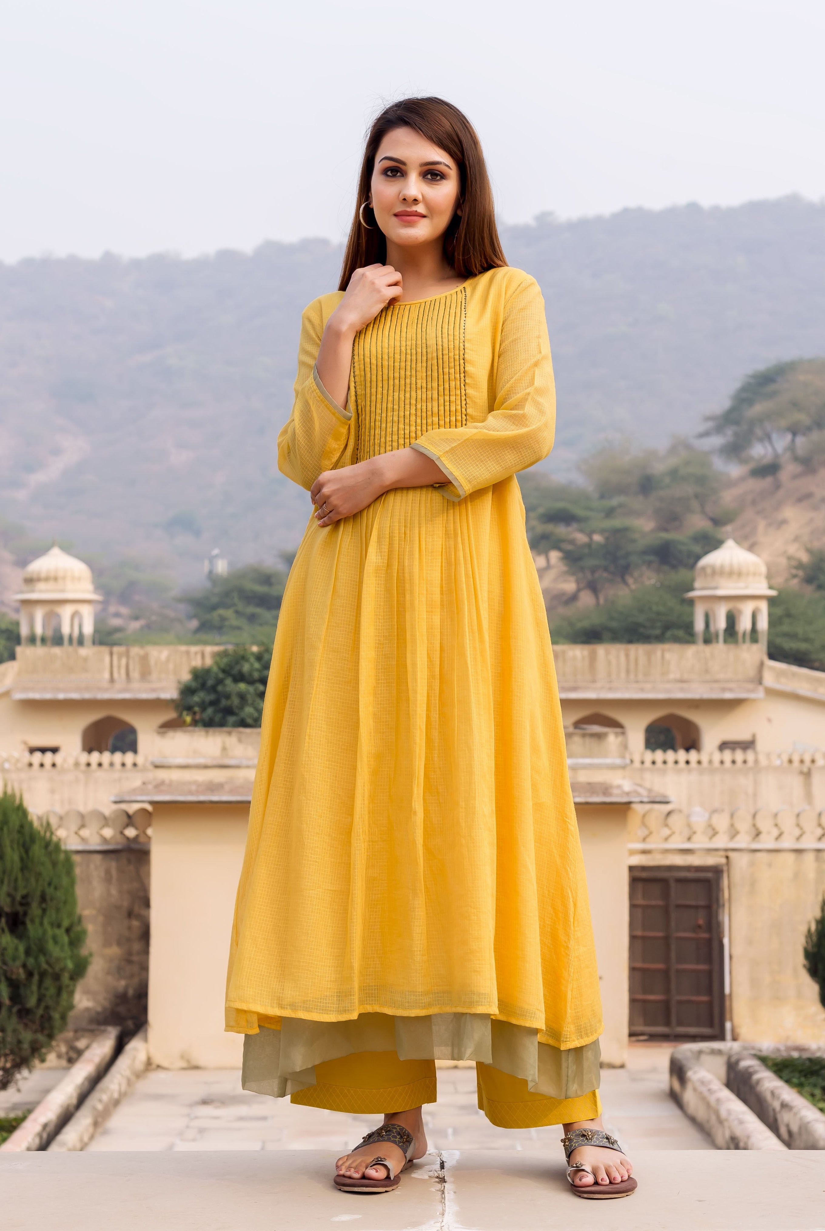 Woman models a honey yellow anarkali kurta with a pleated yoke and subtle texture.