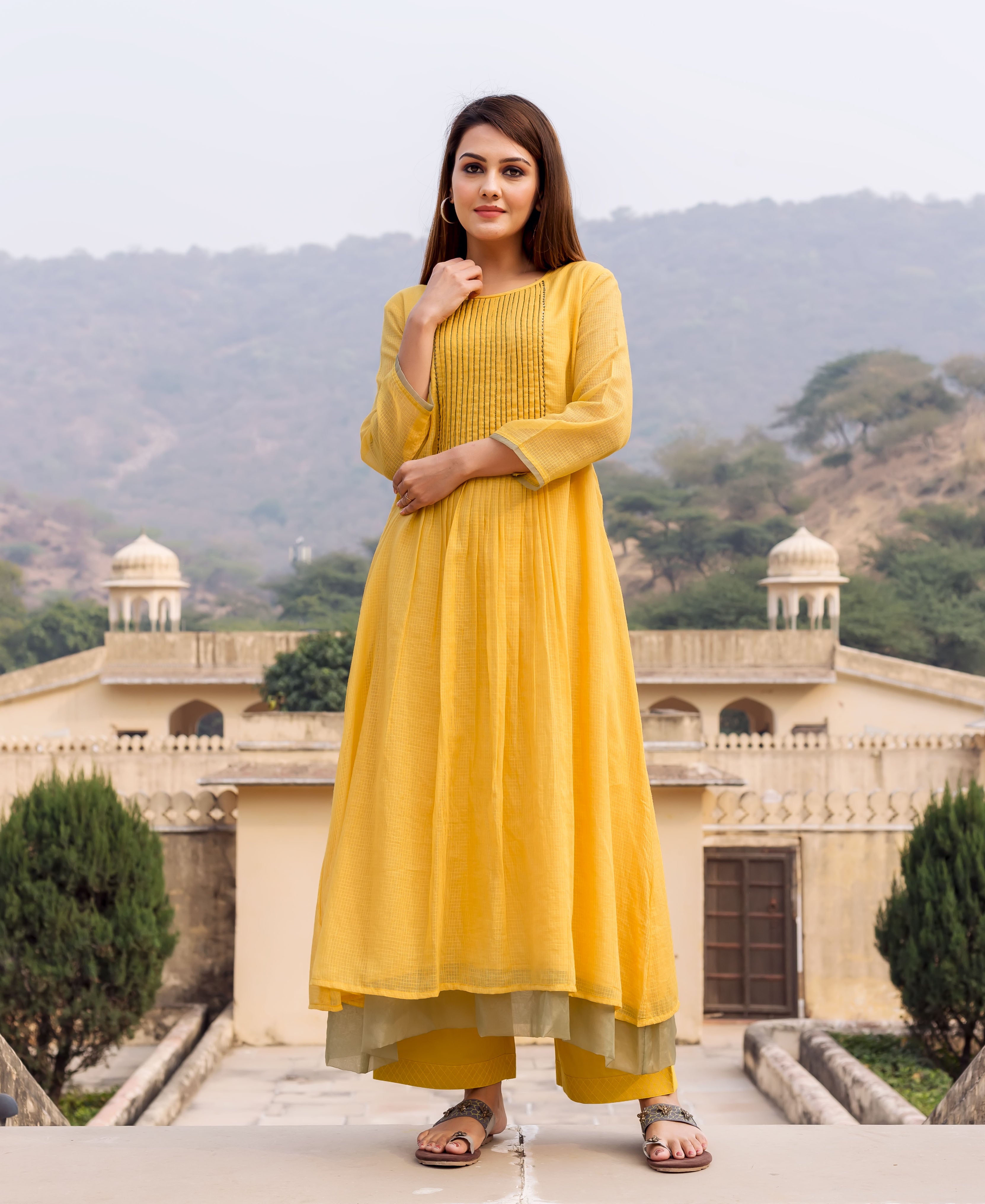 Woman models a honey yellow anarkali kurta with a pleated yoke and subtle texture.