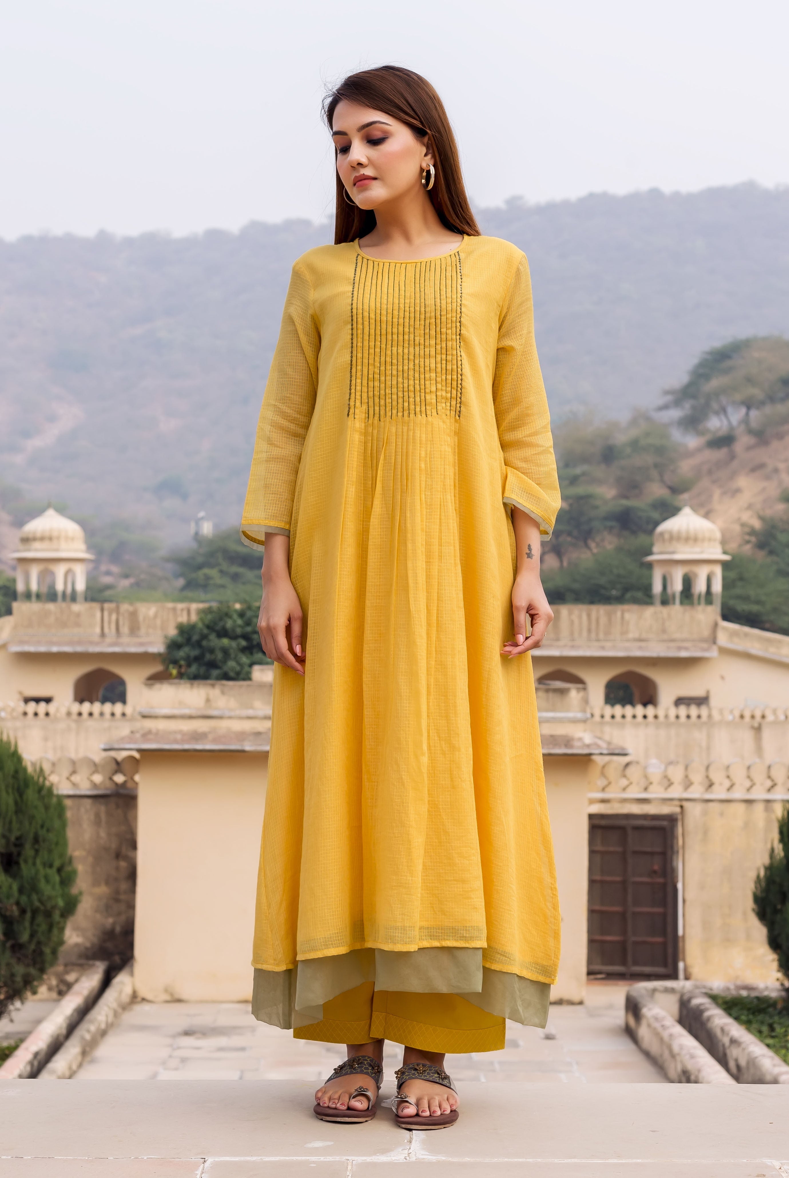 Front view of model wearing a honey yellow kurta, with embroidered pin-tucked yoke, and green layered pants.