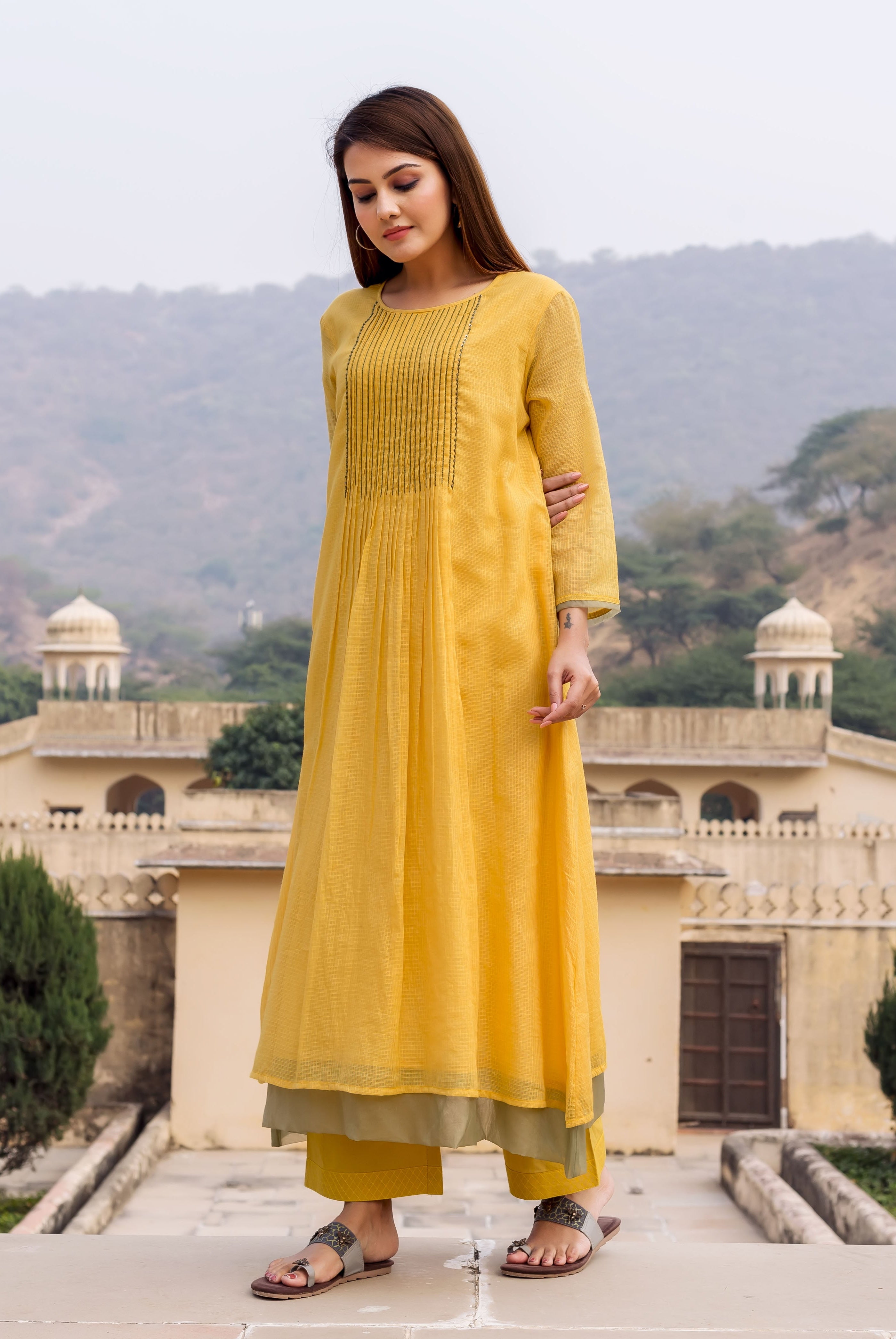 Model wearing a honey yellow embroidered kurta, olive green pants, and brown sandals.