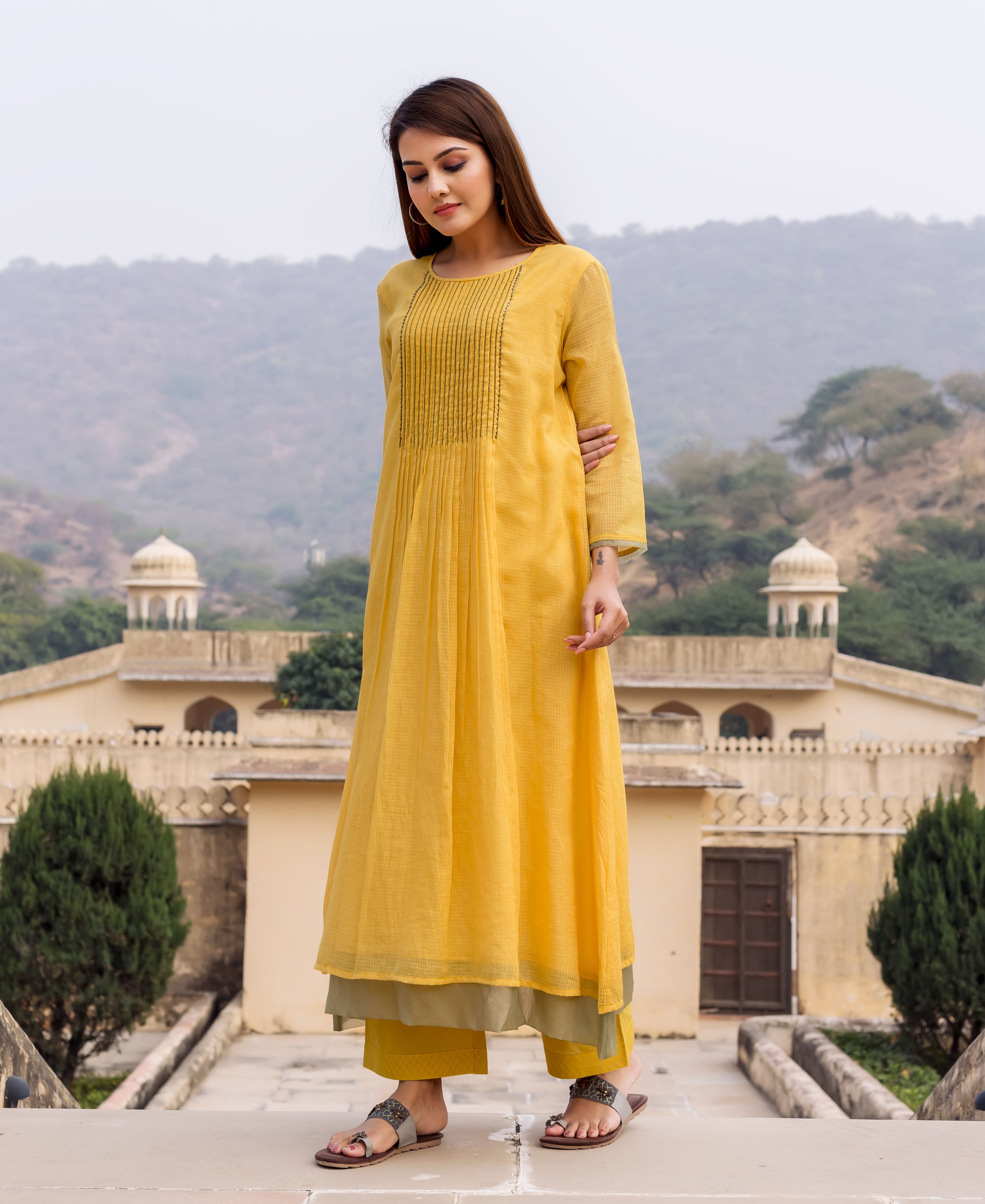 Model wearing a honey yellow embroidered kurta, olive green pants, and brown sandals.