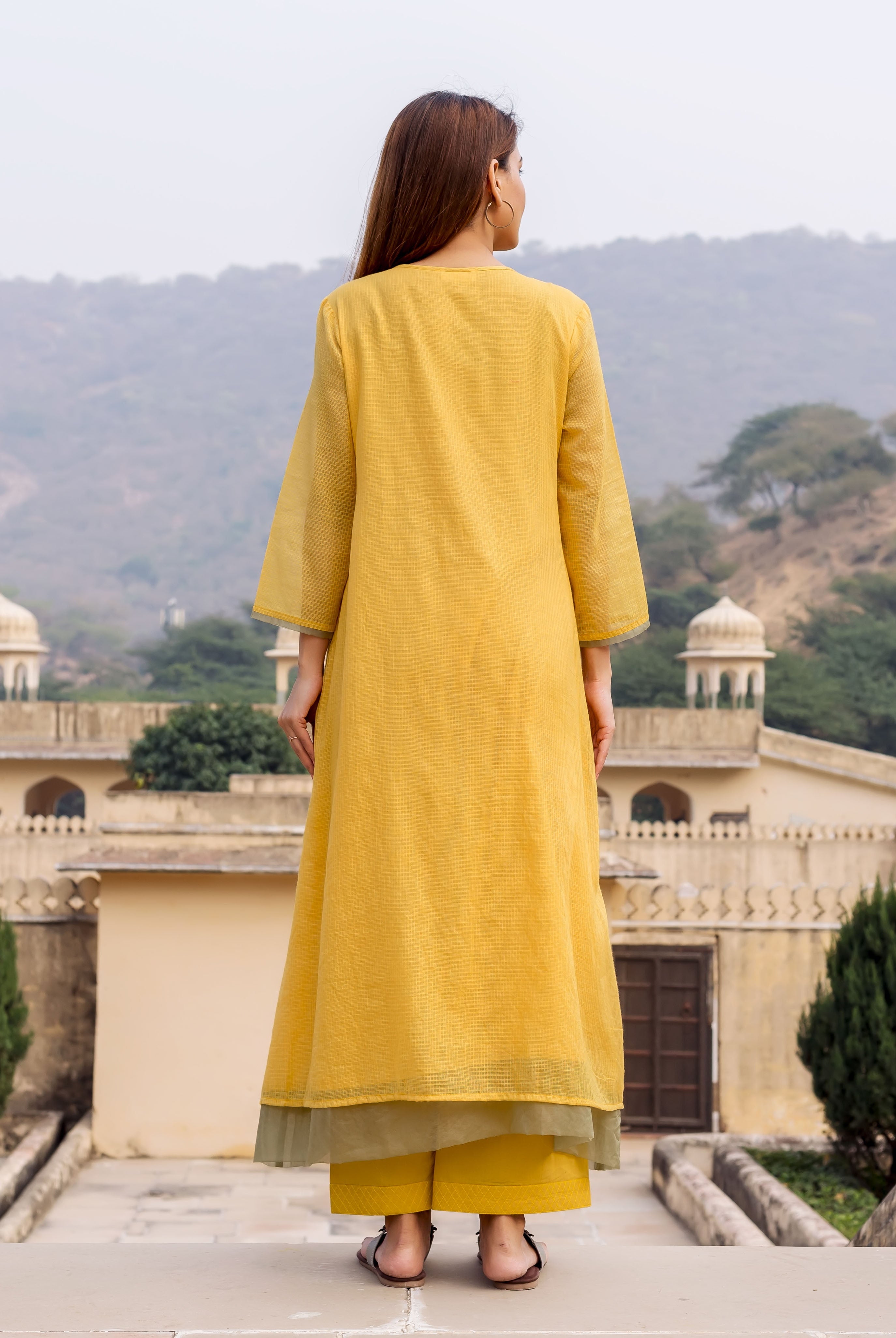 Back view of model in honey yellow textured kurta and bottoms with olive green lining.