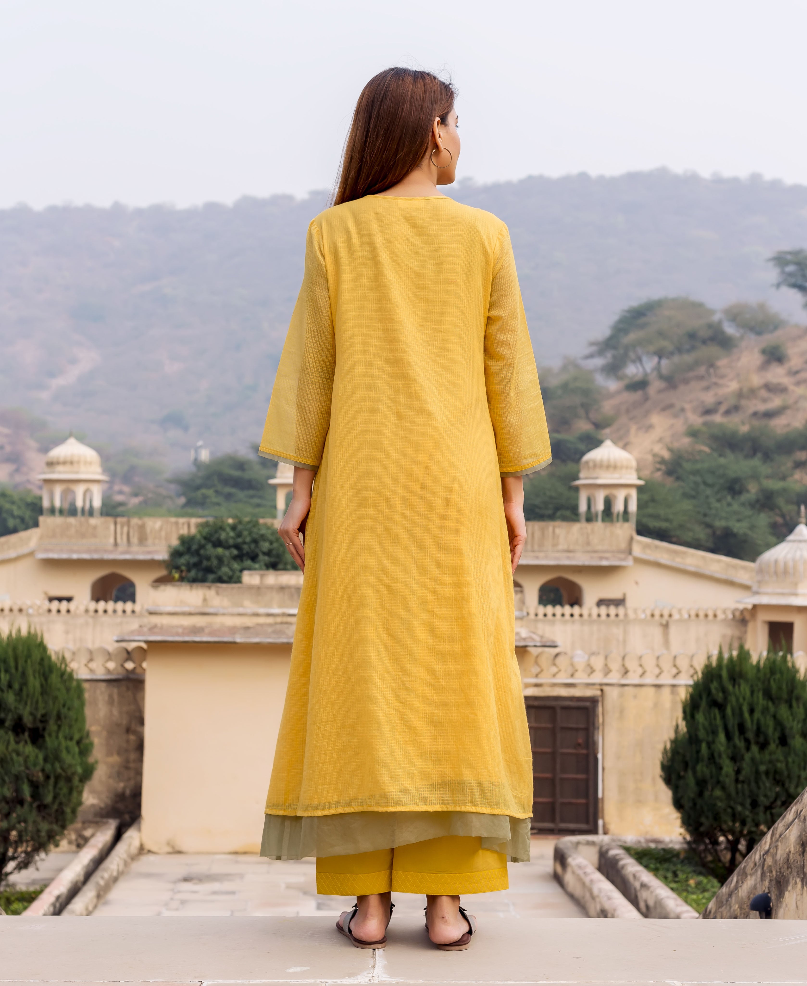 Back view of model in honey yellow textured kurta and bottoms with olive green lining.