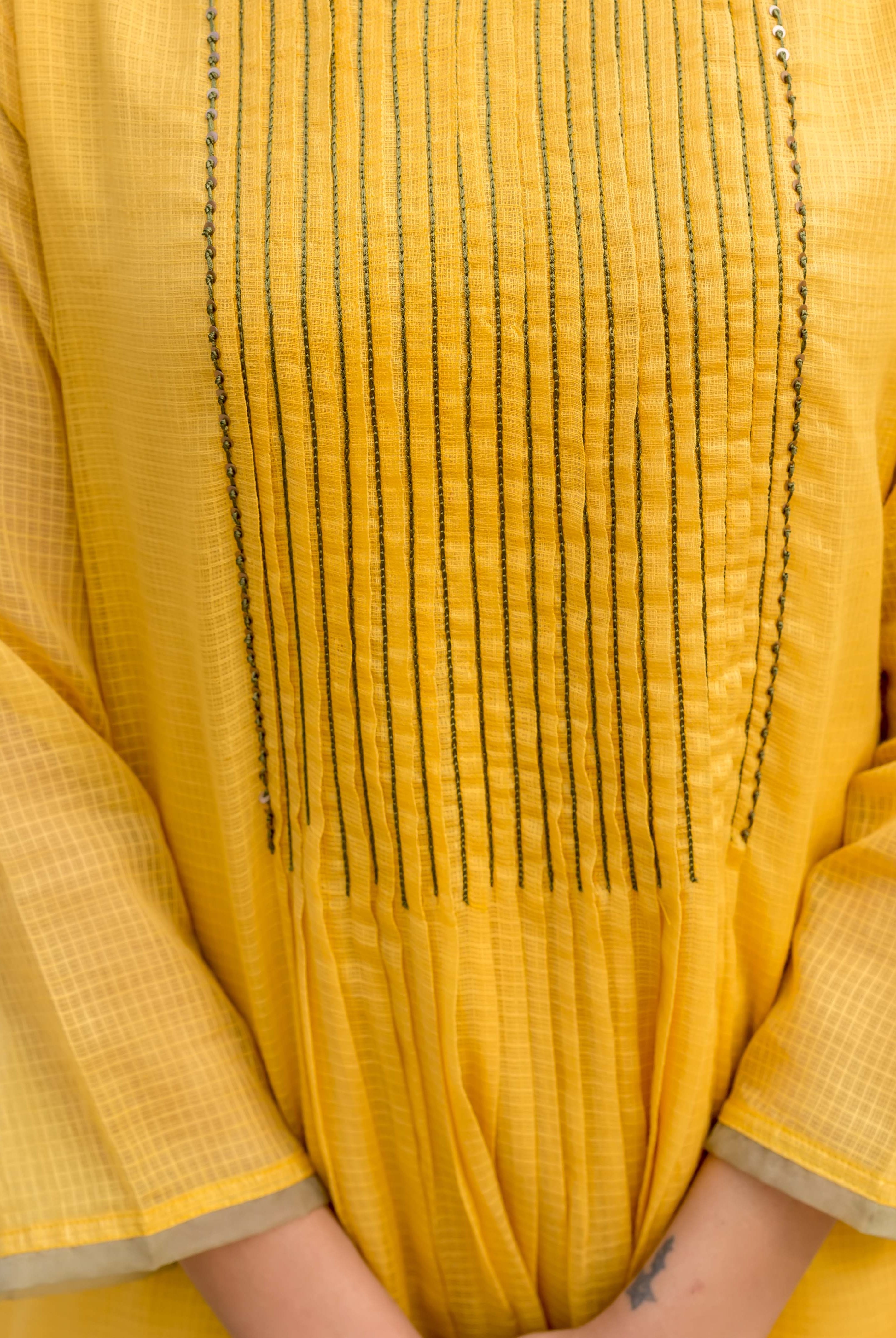 Close-up front of honey yellow kurta on model, with pintucks, fine embroidery, and grid fabric.