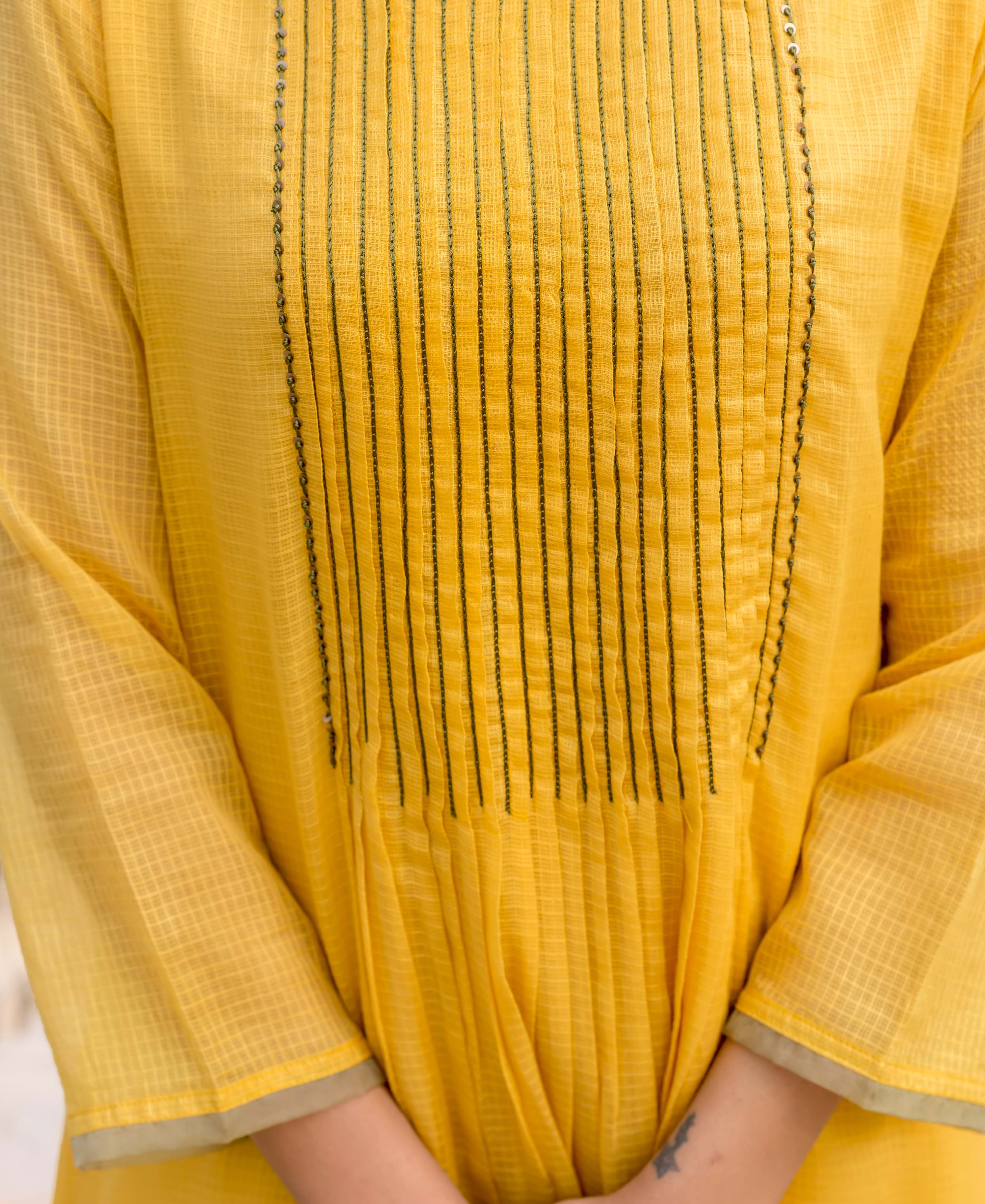 Close-up front of honey yellow kurta on model, with pintucks, fine embroidery, and grid fabric.