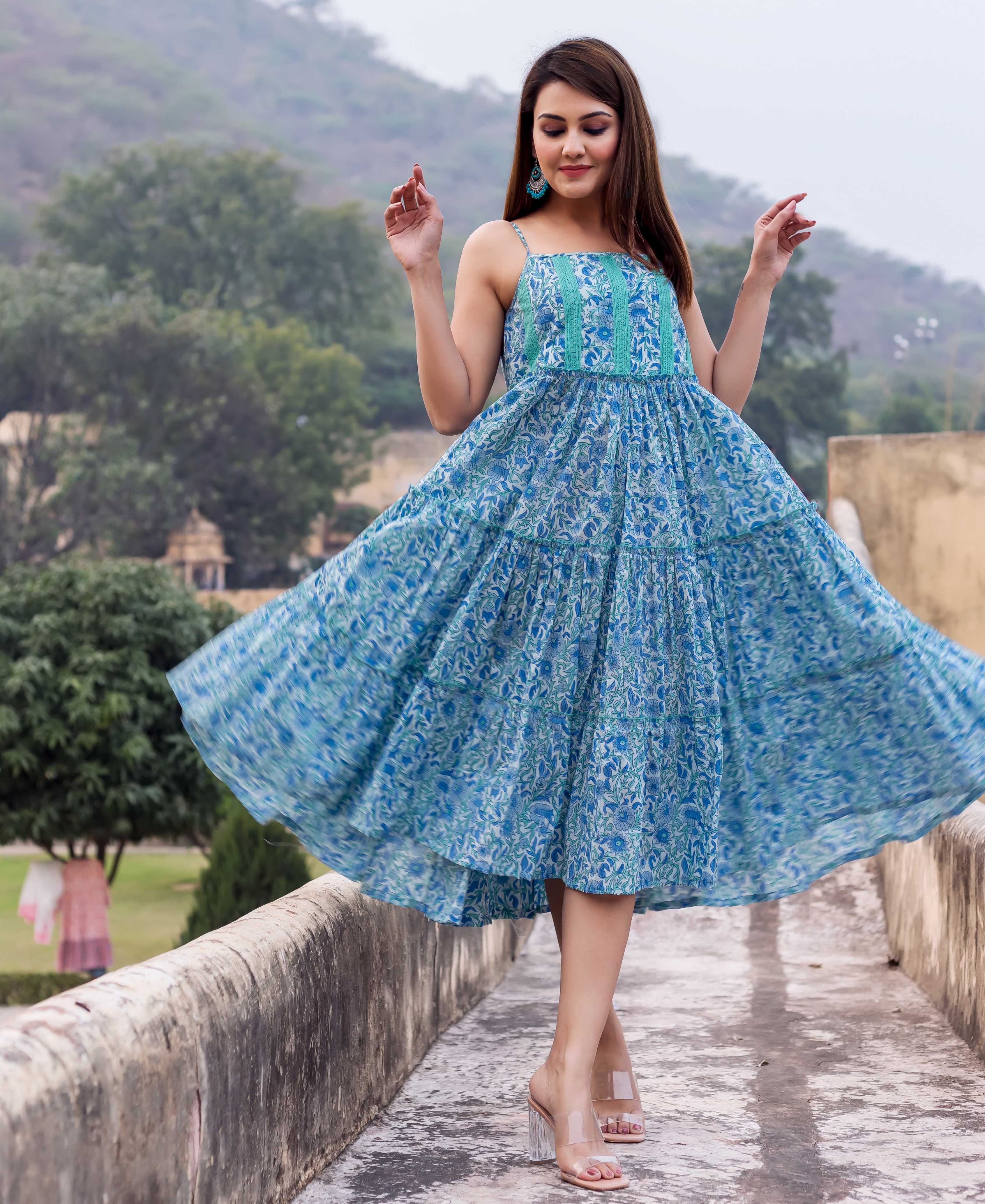 A woman in a blue and white floral sundress with a full skirt, standing on a stone wall.