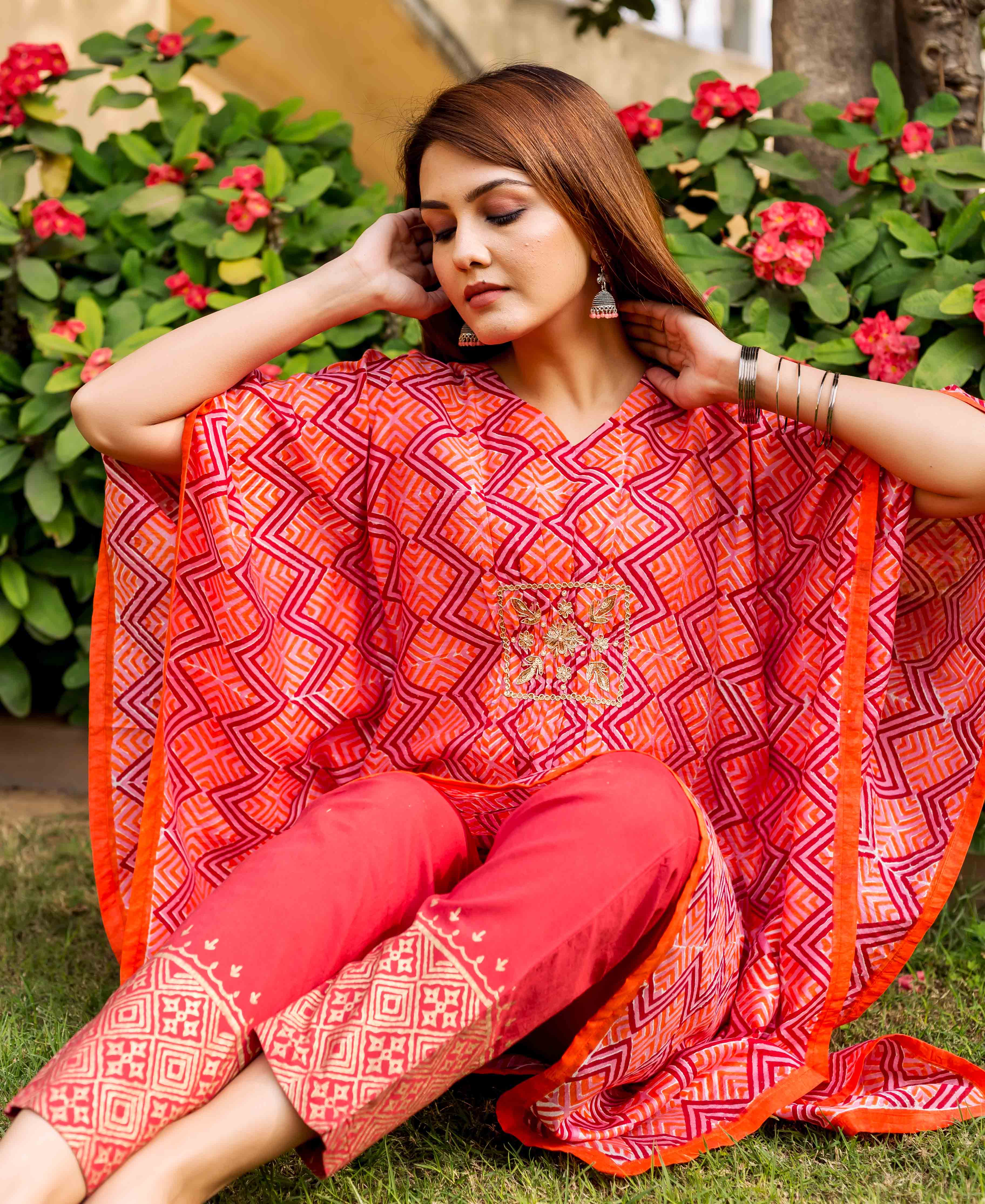 Sitting model in a red-orange zig-zag printed and embroidered kaftan with matching pants.