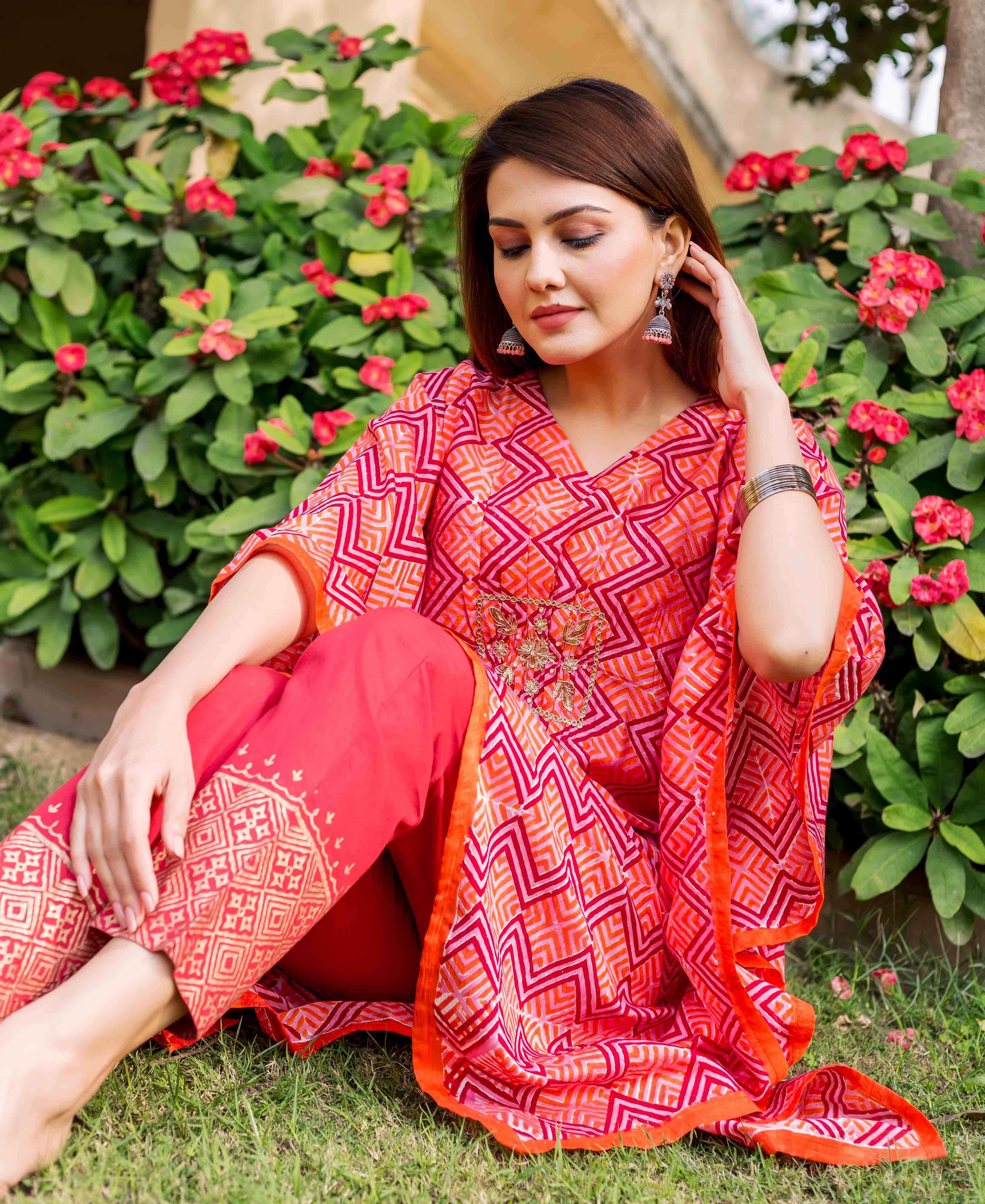 Model sitting in a red-orange zig-zag printed kaftan with golden embroidery and solid pants.