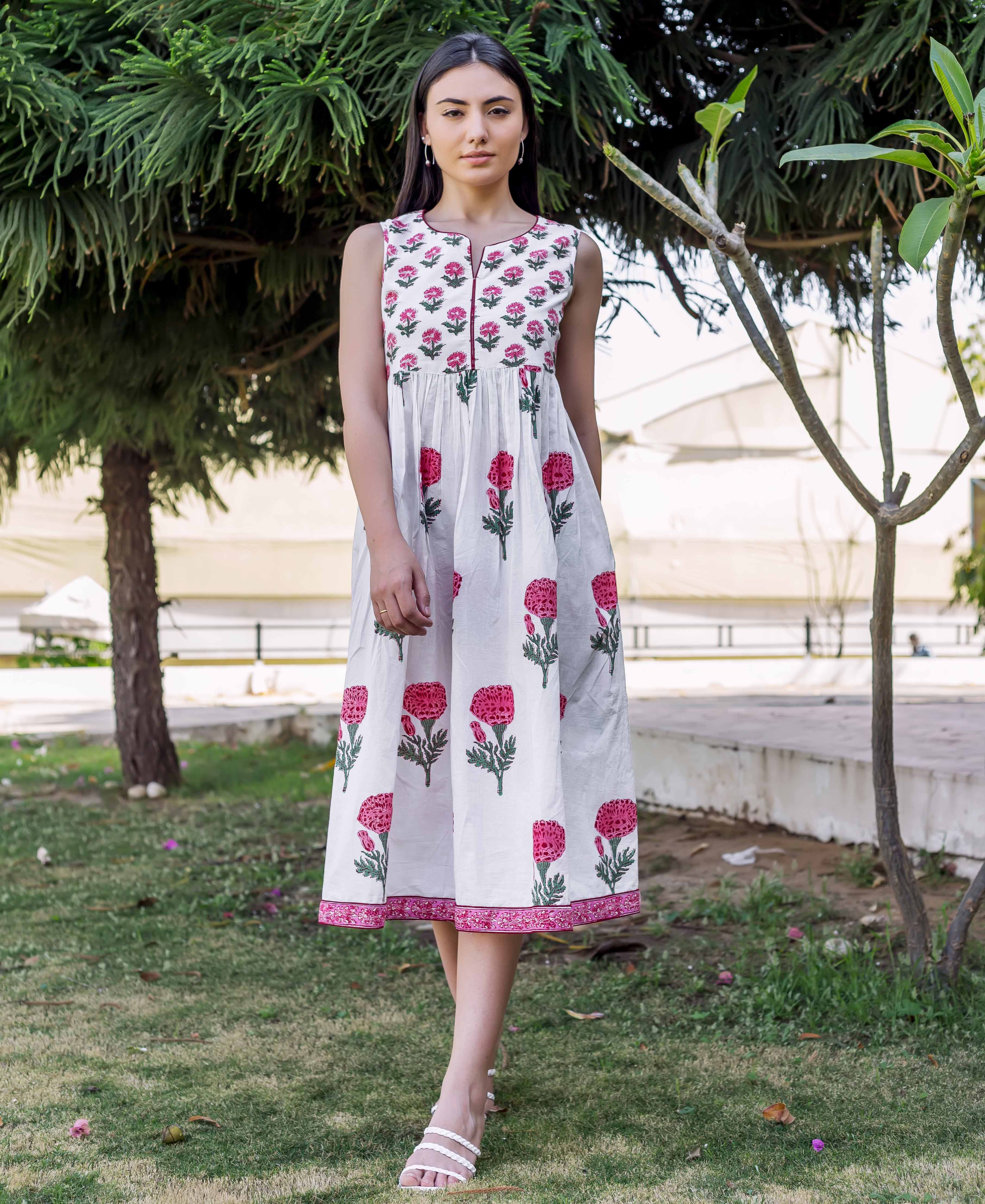 Standing model in white gathered sleeveless midi dress with pink marigold block print.