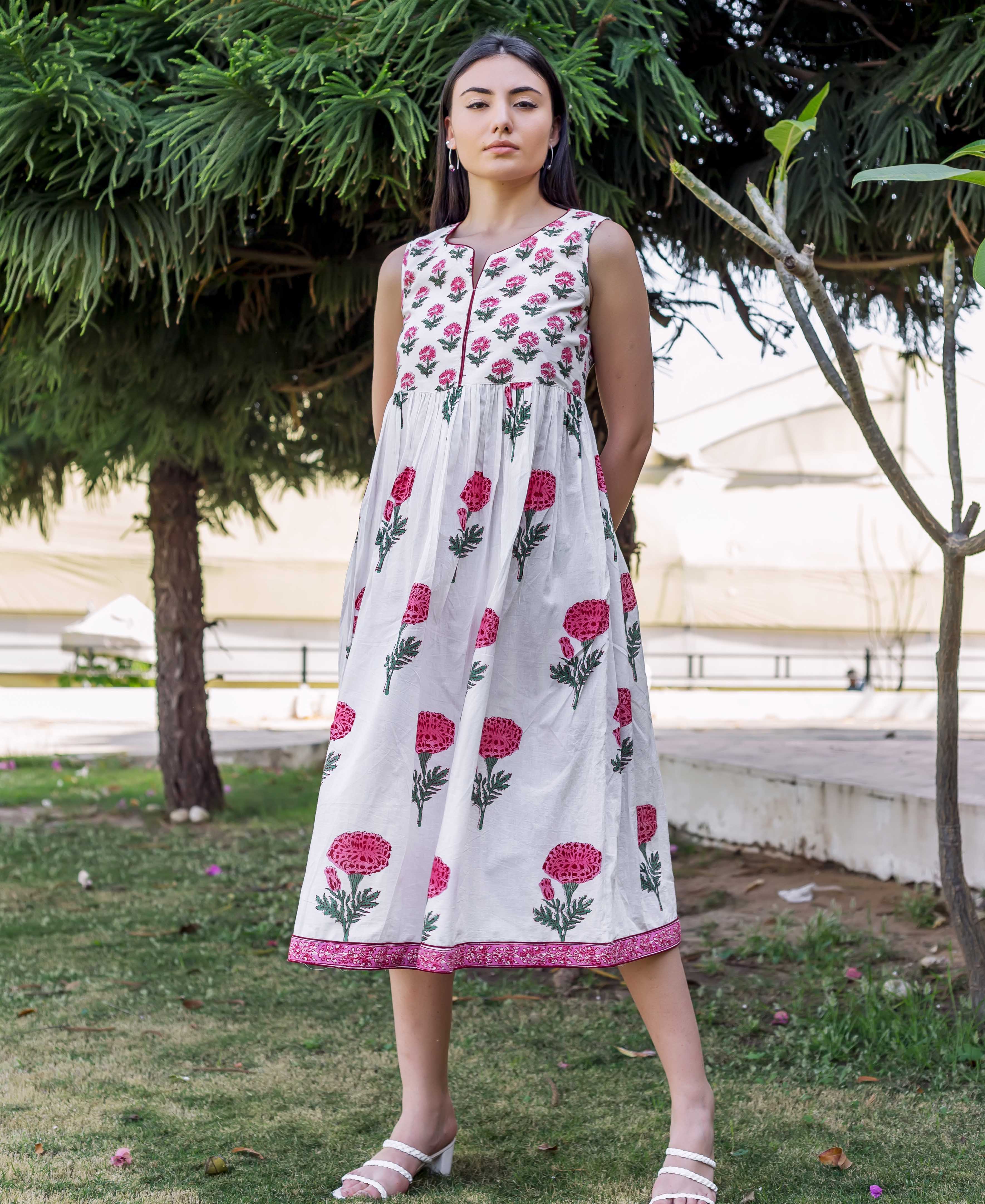 A woman wearing a white dress with pink marigold flowers and green leaves.