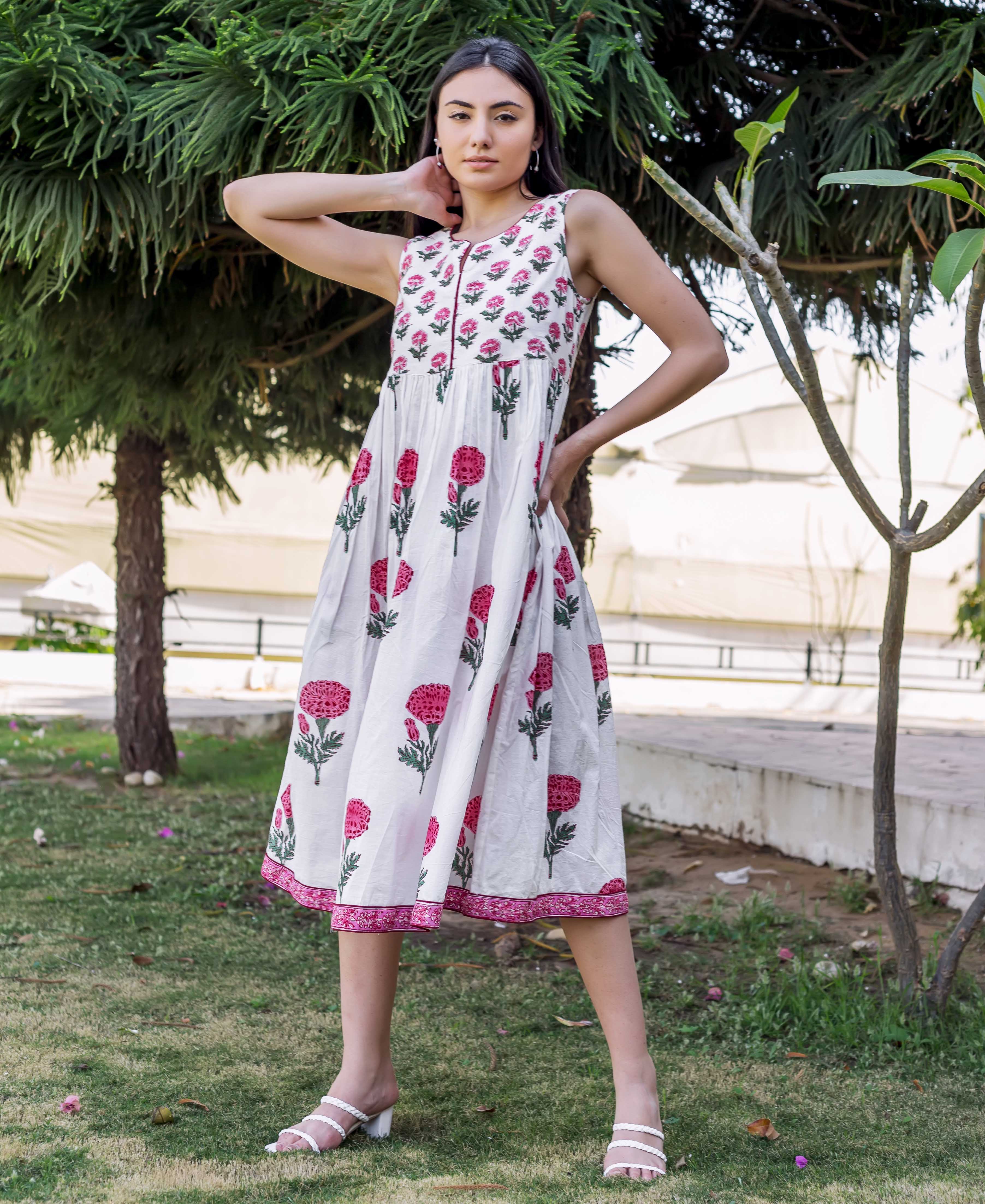 Woman in white sleeveless midi dress with pink marigold block prints, standing outdoors.