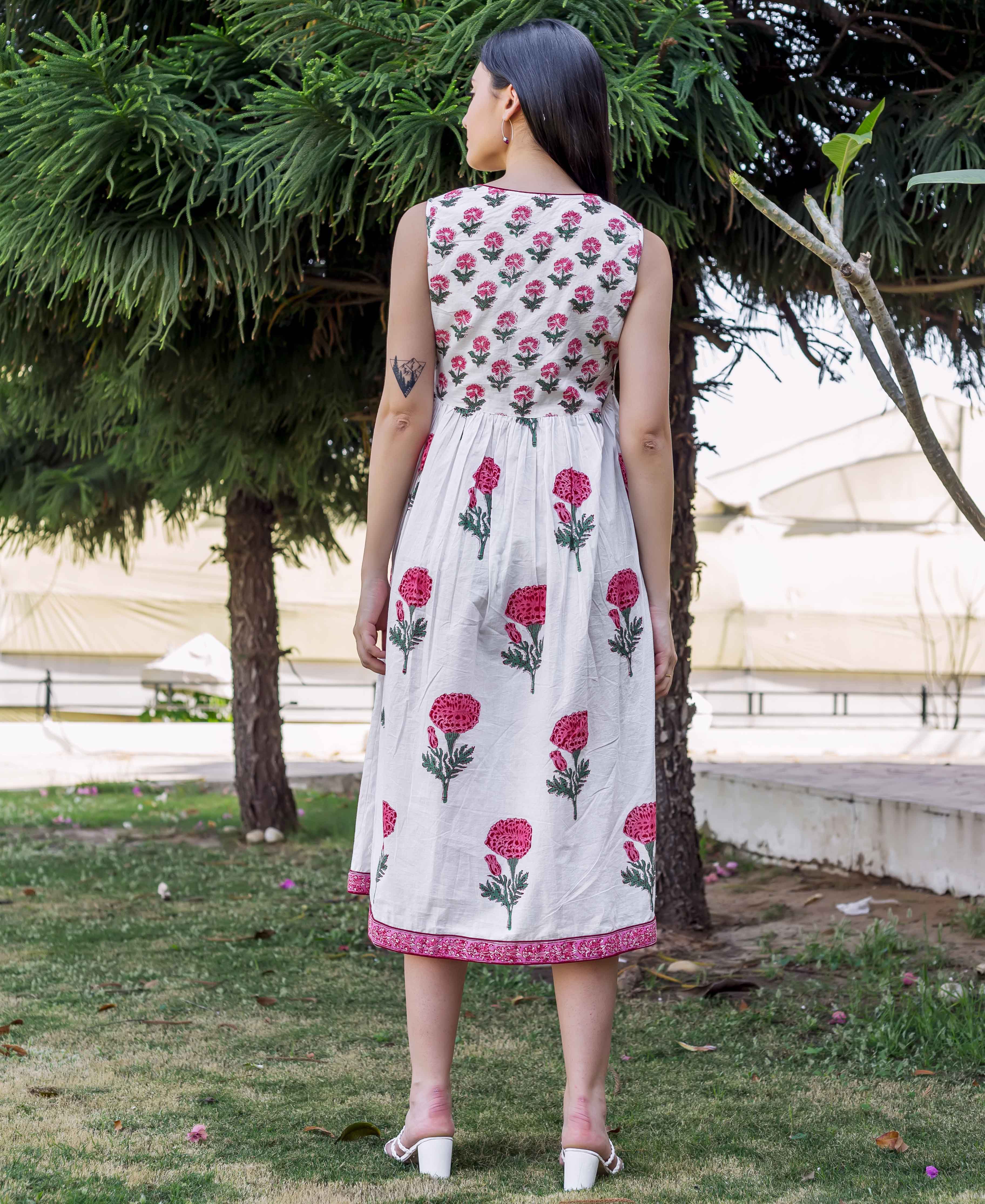Back view of model wearing a white sleeveless midi dress with pink marigold block print.