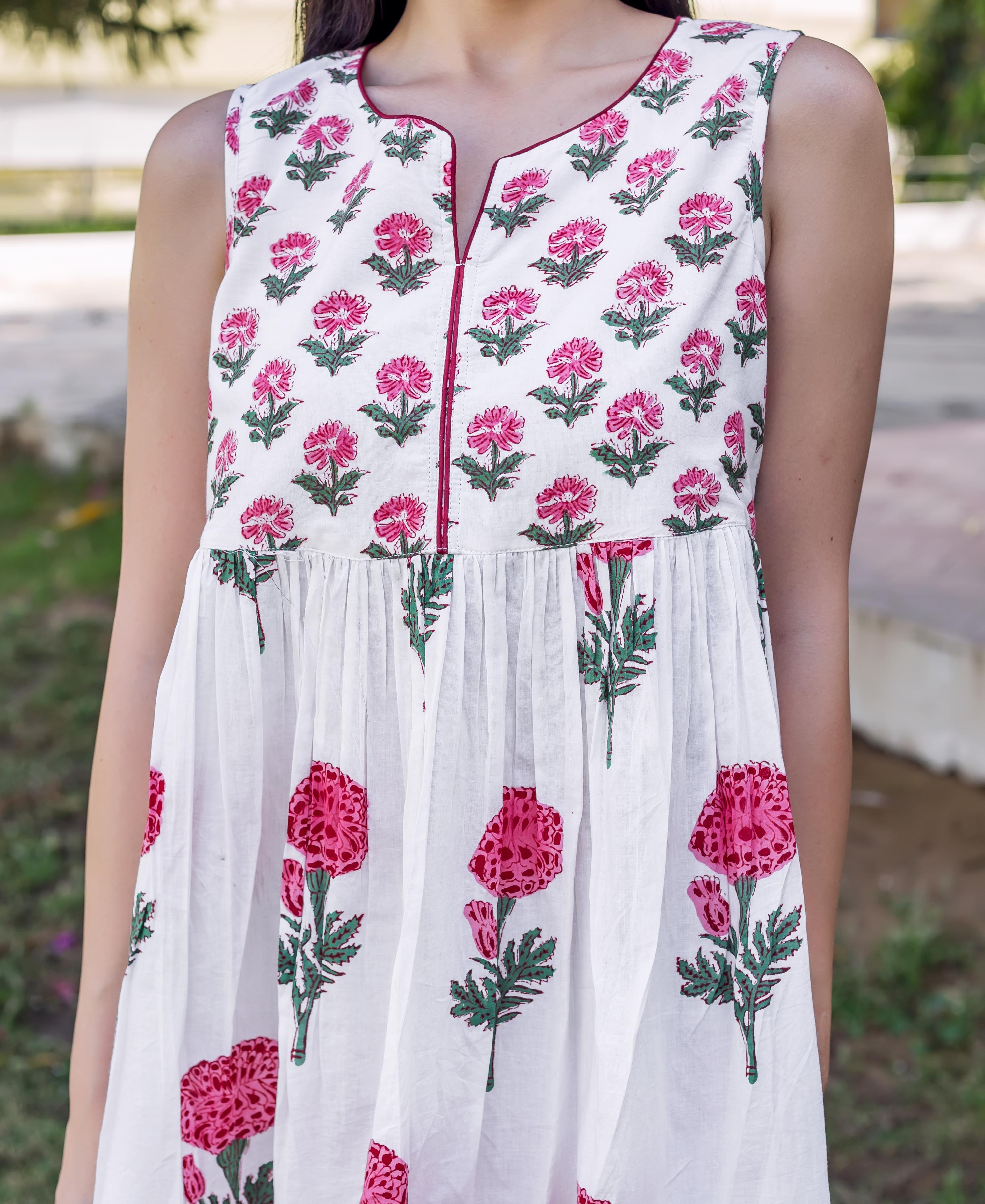 A woman wearing a white dress with pink marigold flowers and green leaves.