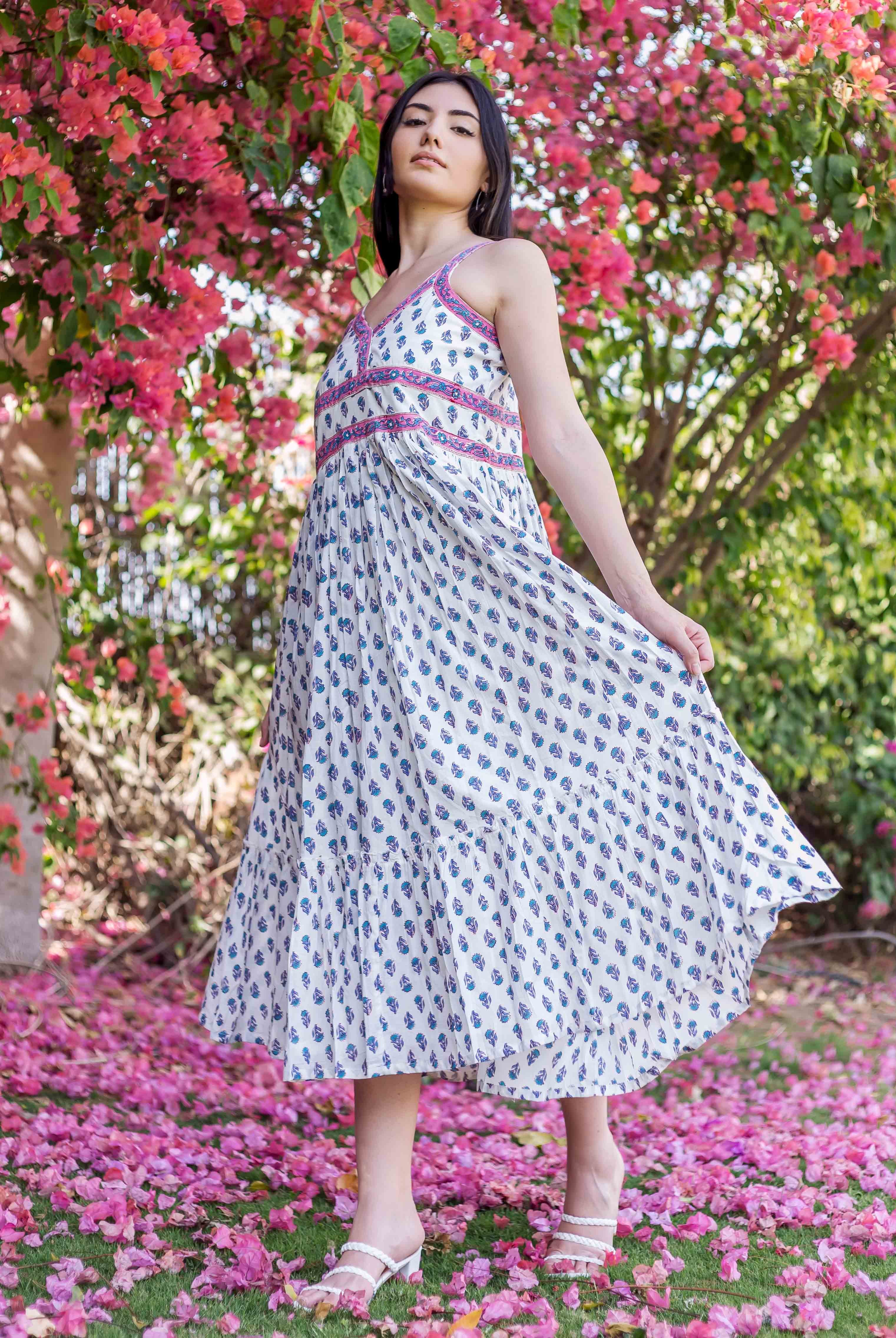Woman wears white block-printed midi dress with blue-purple motifs and pink-purple bodice.