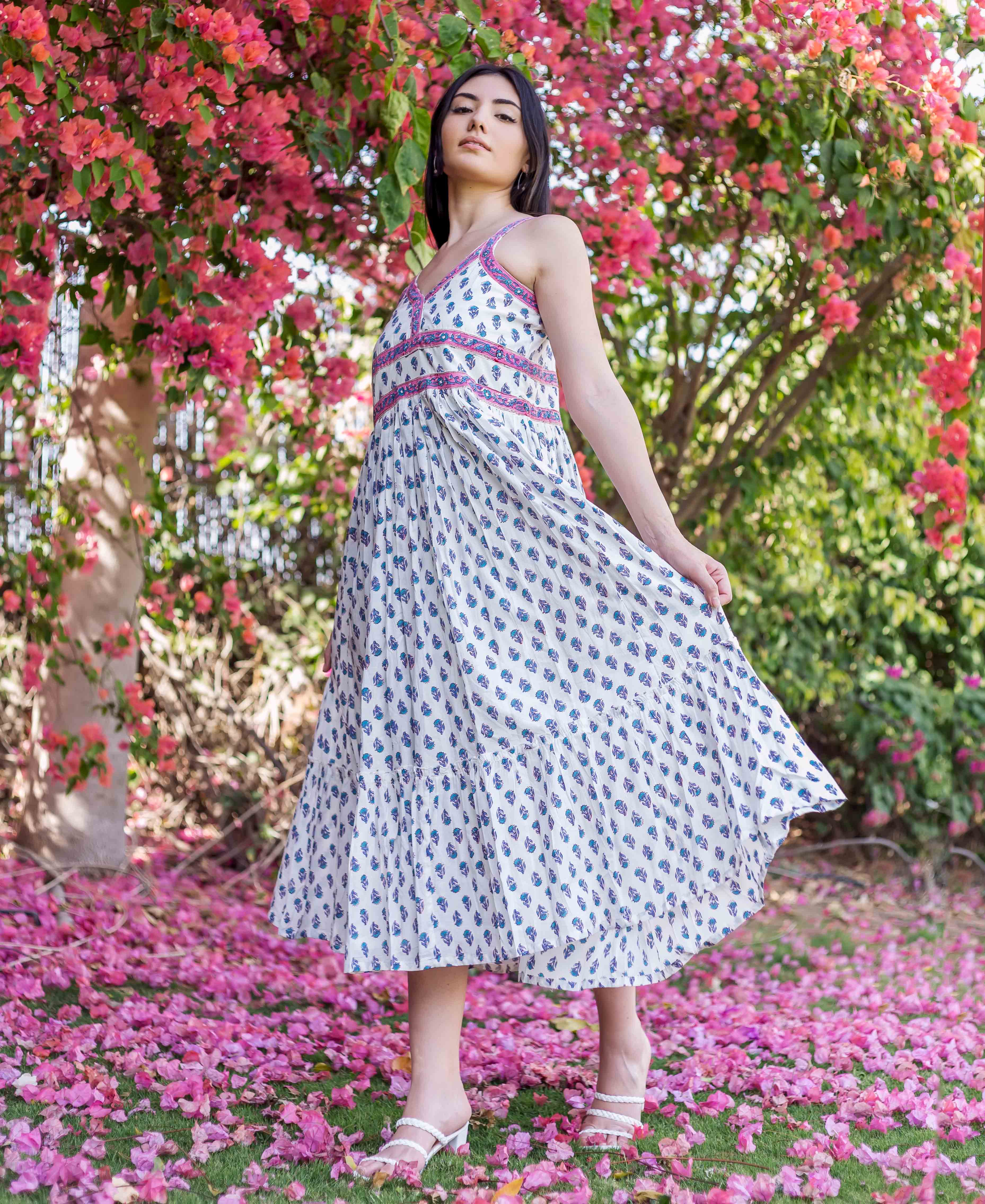 Woman wears white block-printed midi dress with blue-purple motifs and pink-purple bodice.