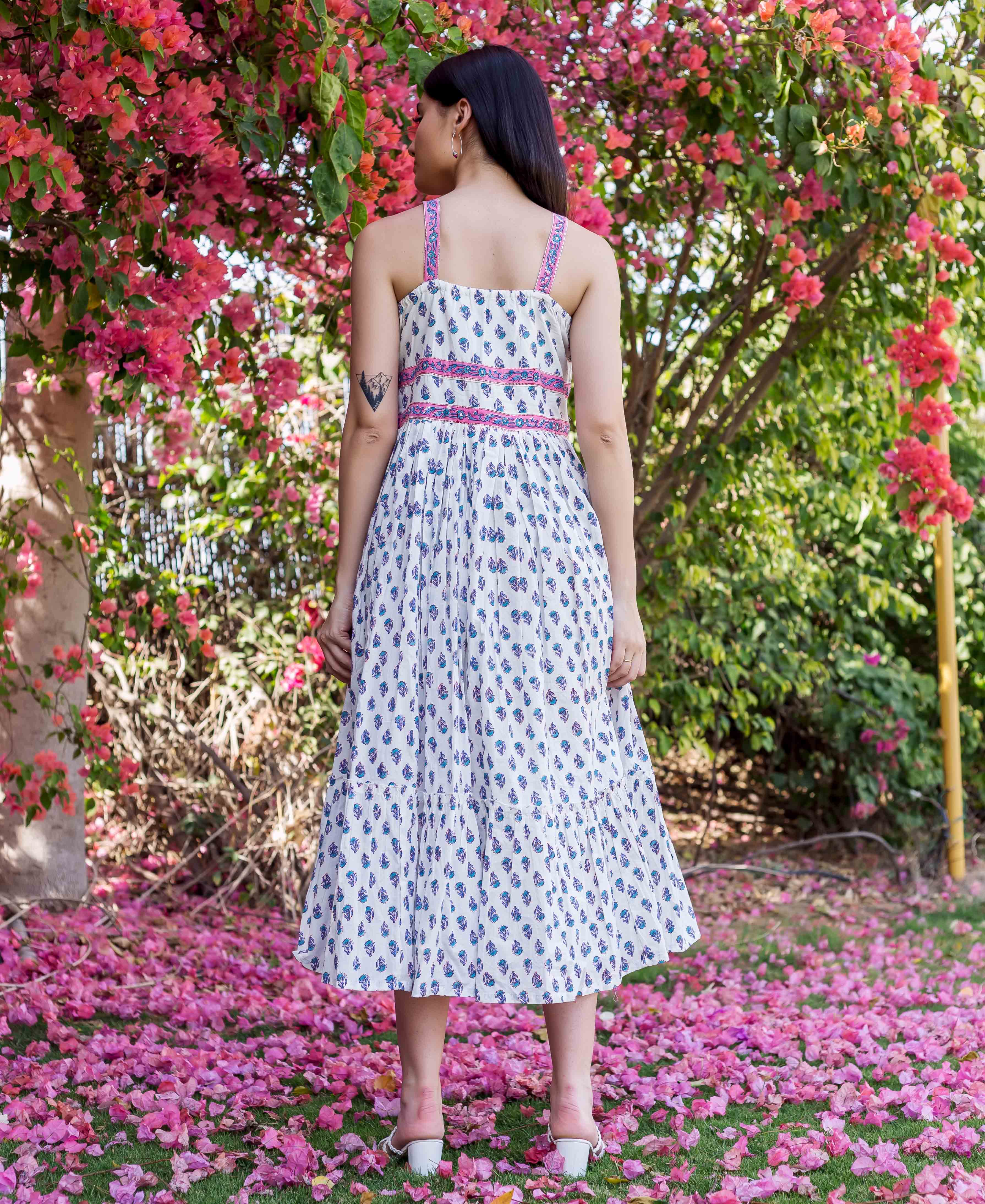 Model from behind in white block print midi dress with pink straps and blue motifs.