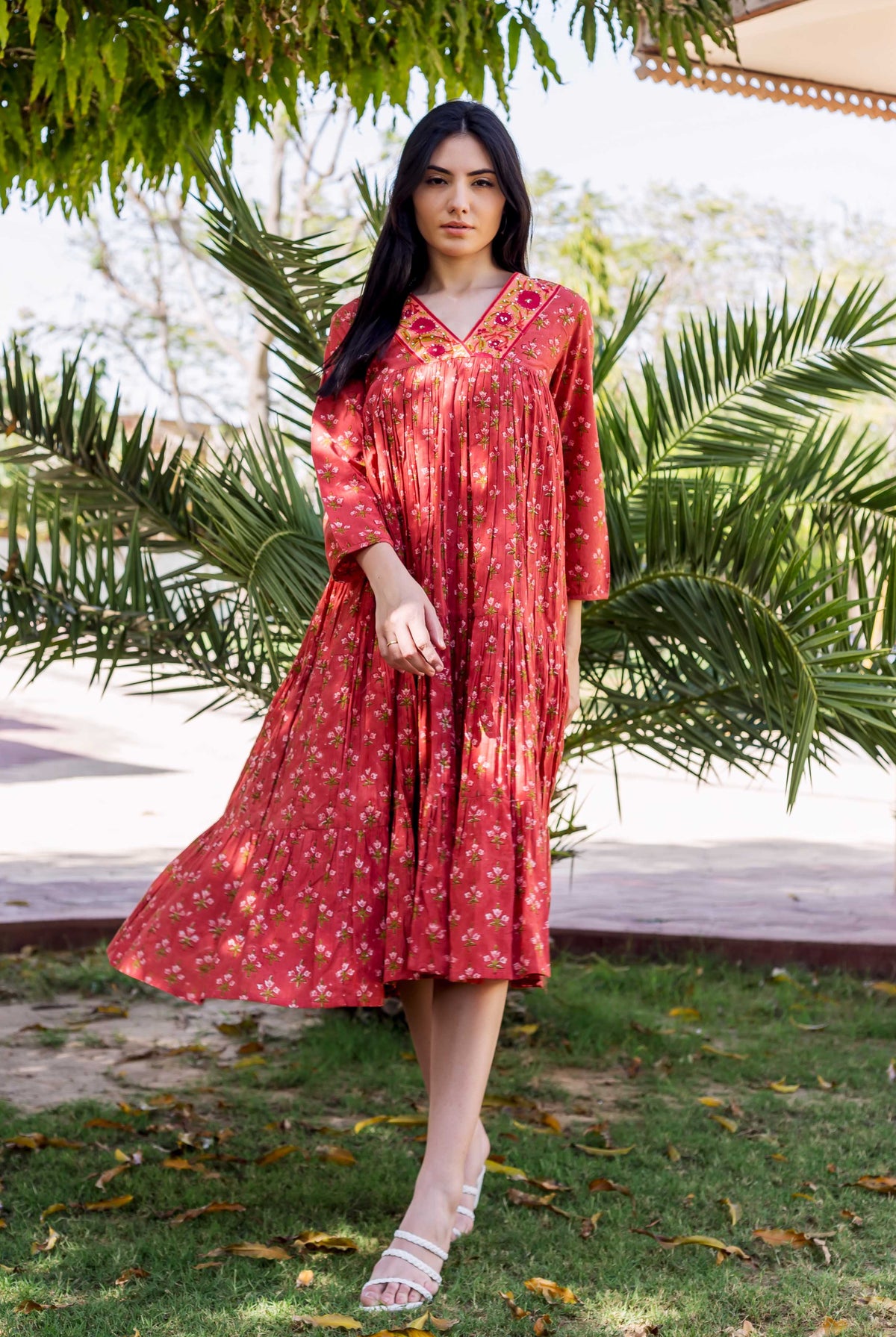 Full-body shot of model in rust-red tiered floral hand-block-printed dress with embroidered neckline.