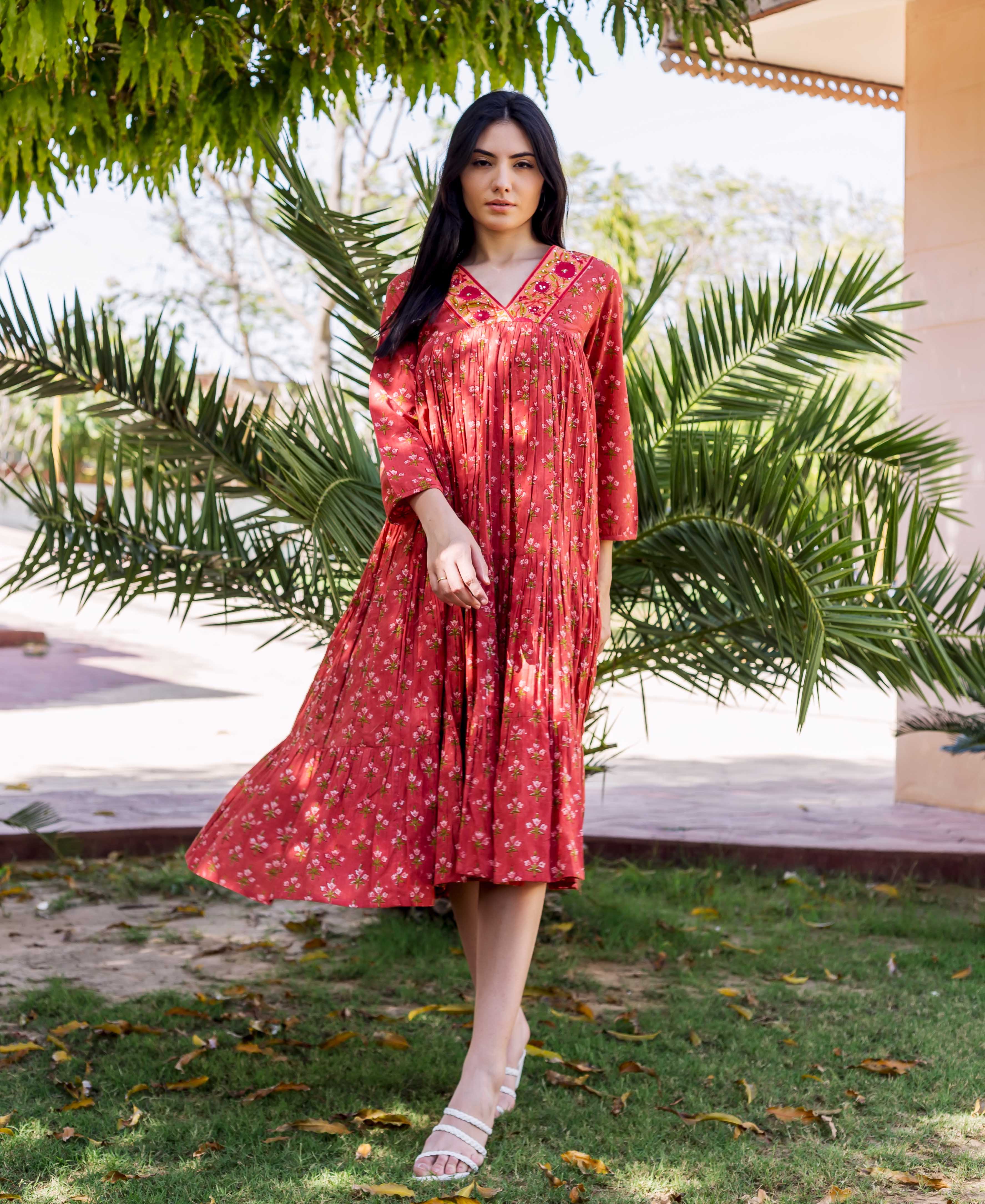 Full-body shot of model in rust-red tiered floral hand-block-printed dress with embroidered neckline.