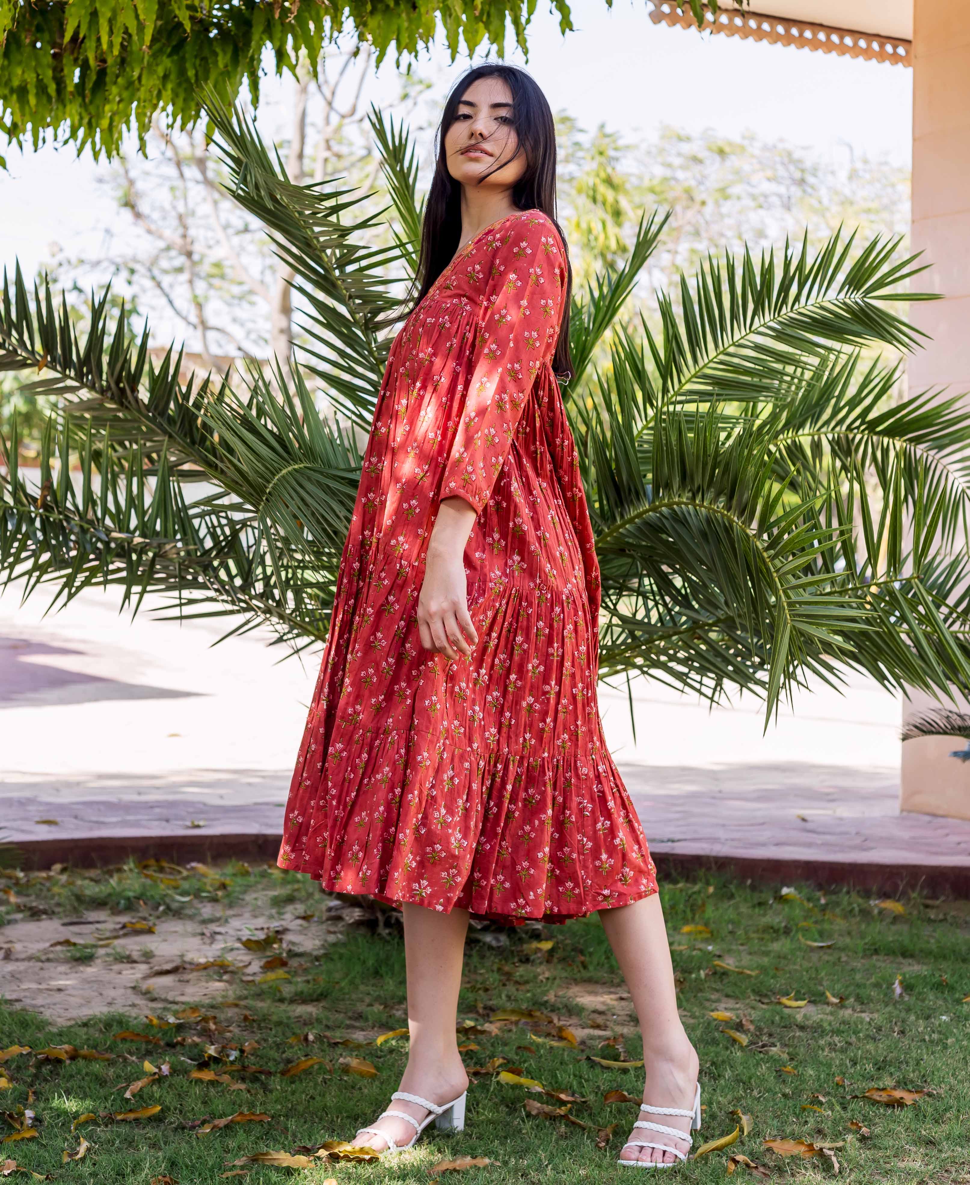 Model wears a coral-red tiered midi dress with small floral prints, outdoors.