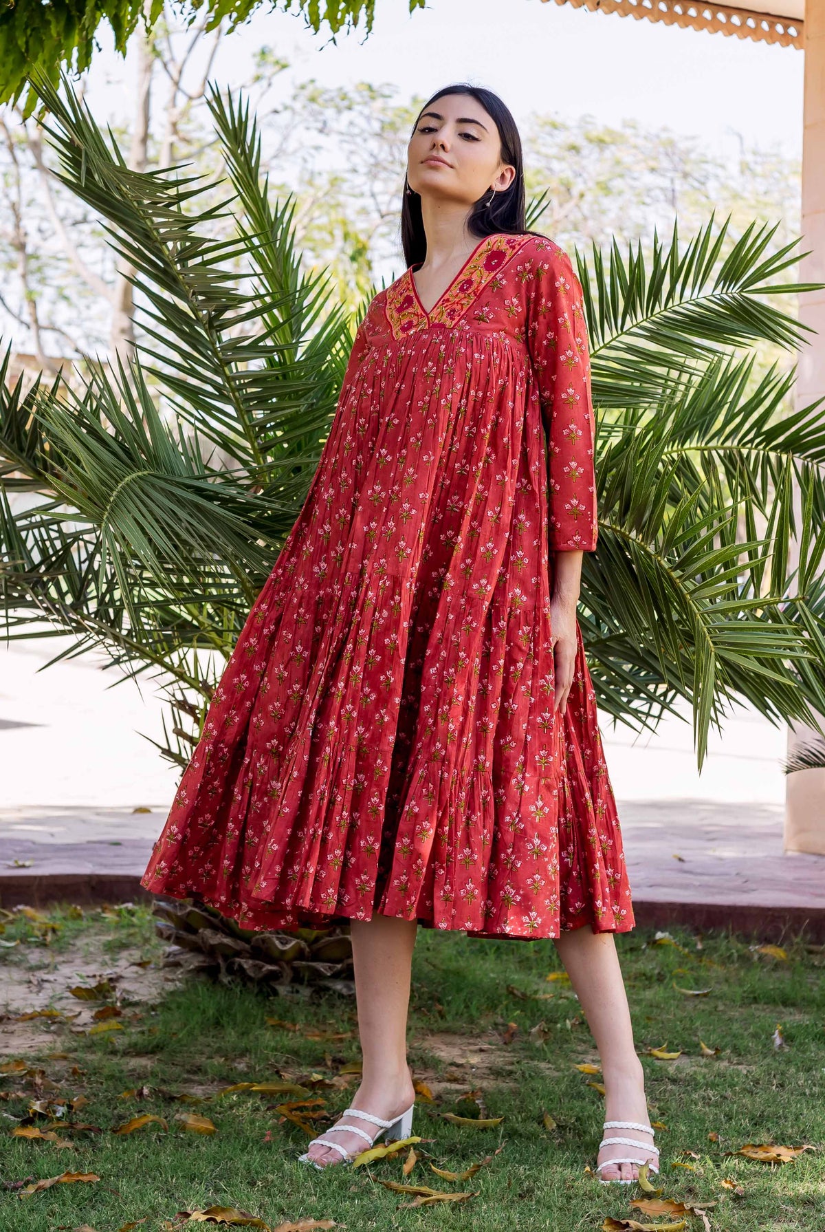 A model wearing a red floral block-printed tiered dress with white heels.