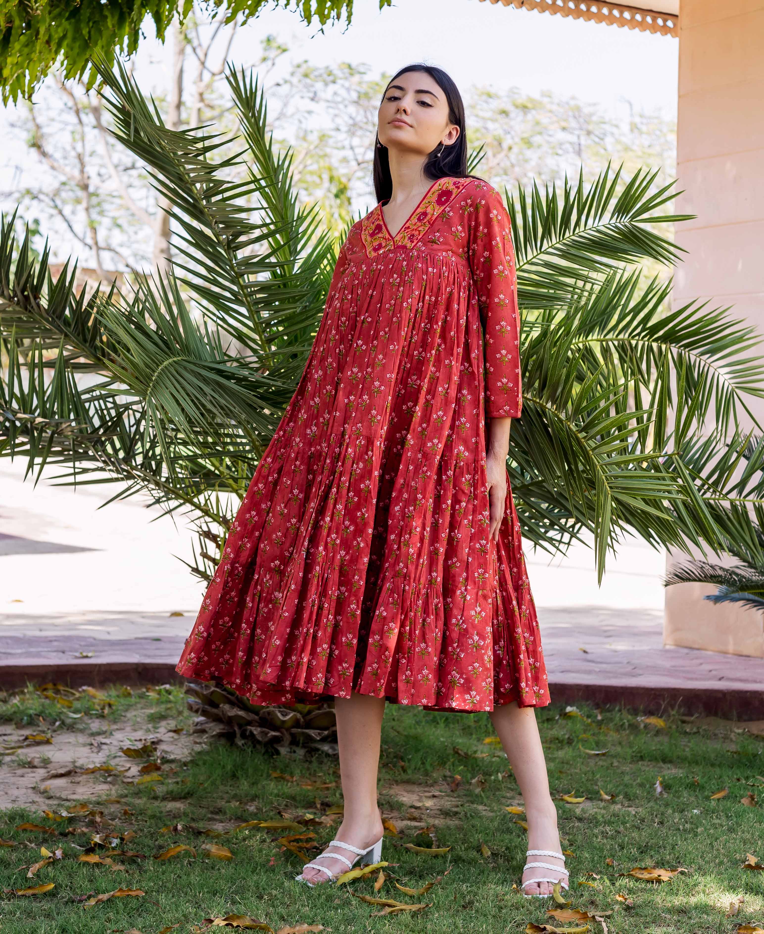 A model wearing a red floral block-printed tiered dress with white heels.