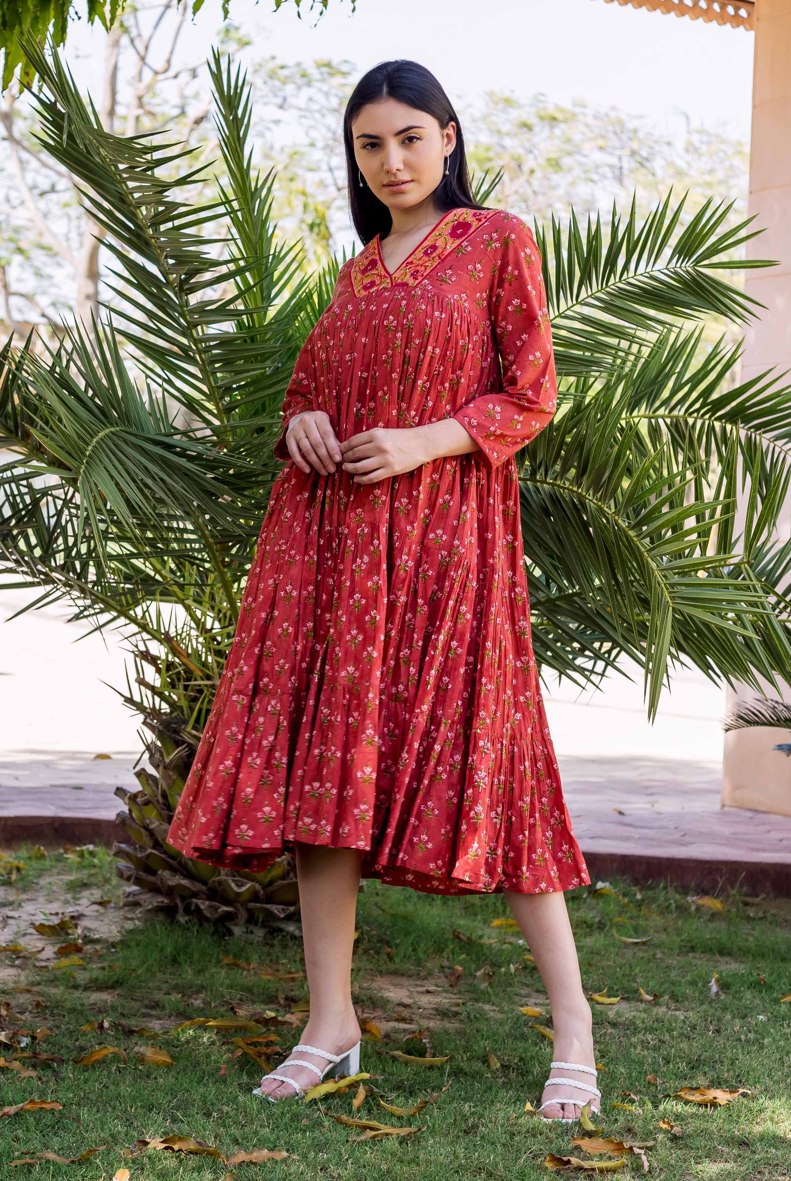 Model wearing a rust red tiered dress with floral block print and embroidered V-neck.