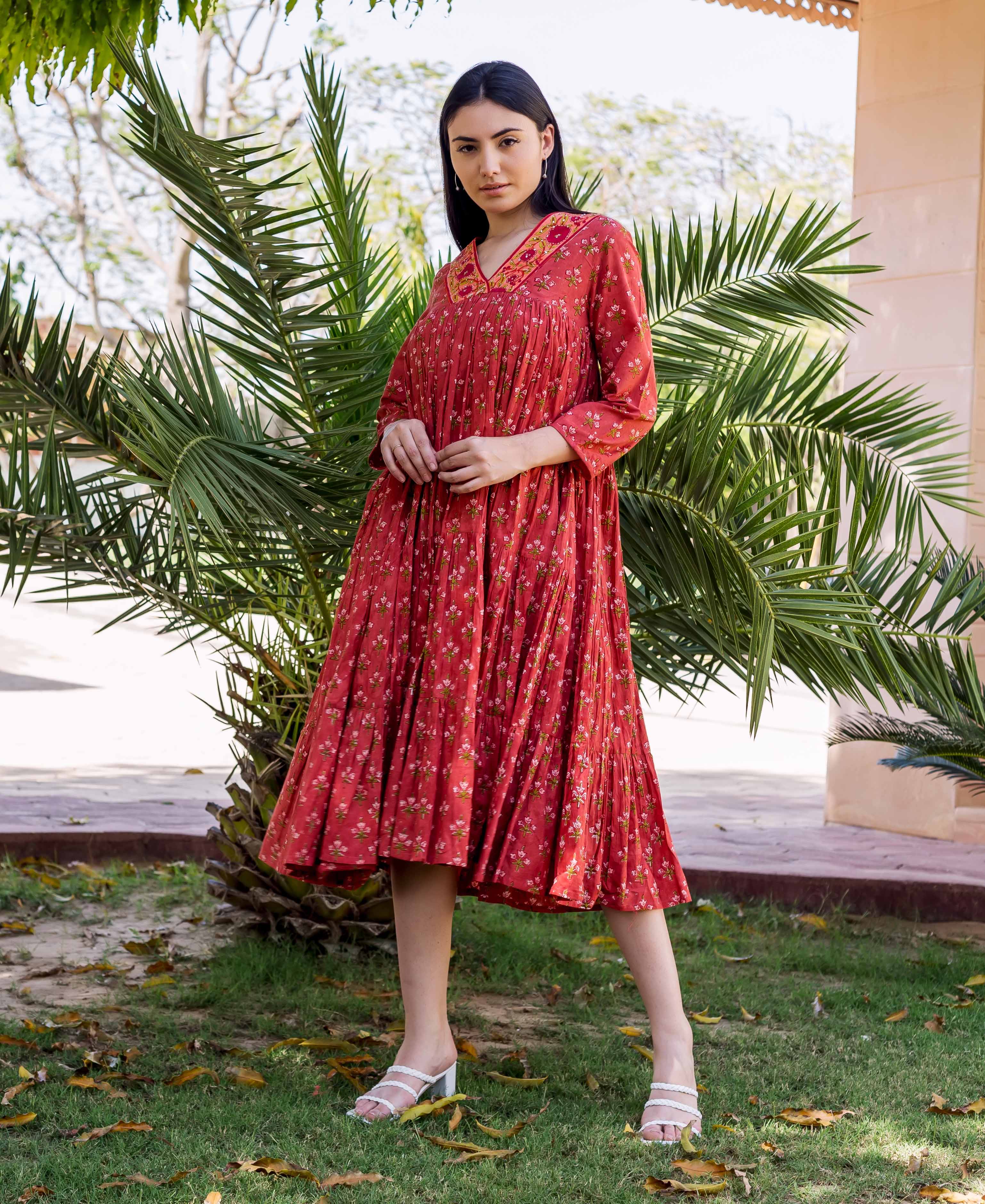Model wearing a rust red tiered dress with floral block print and embroidered V-neck.