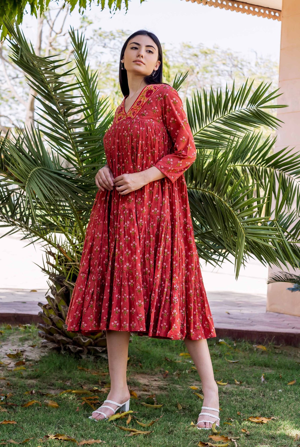 Model in a maroon hand-block-printed tiered dress with delicate floral patterns and an embroidered V-neck.