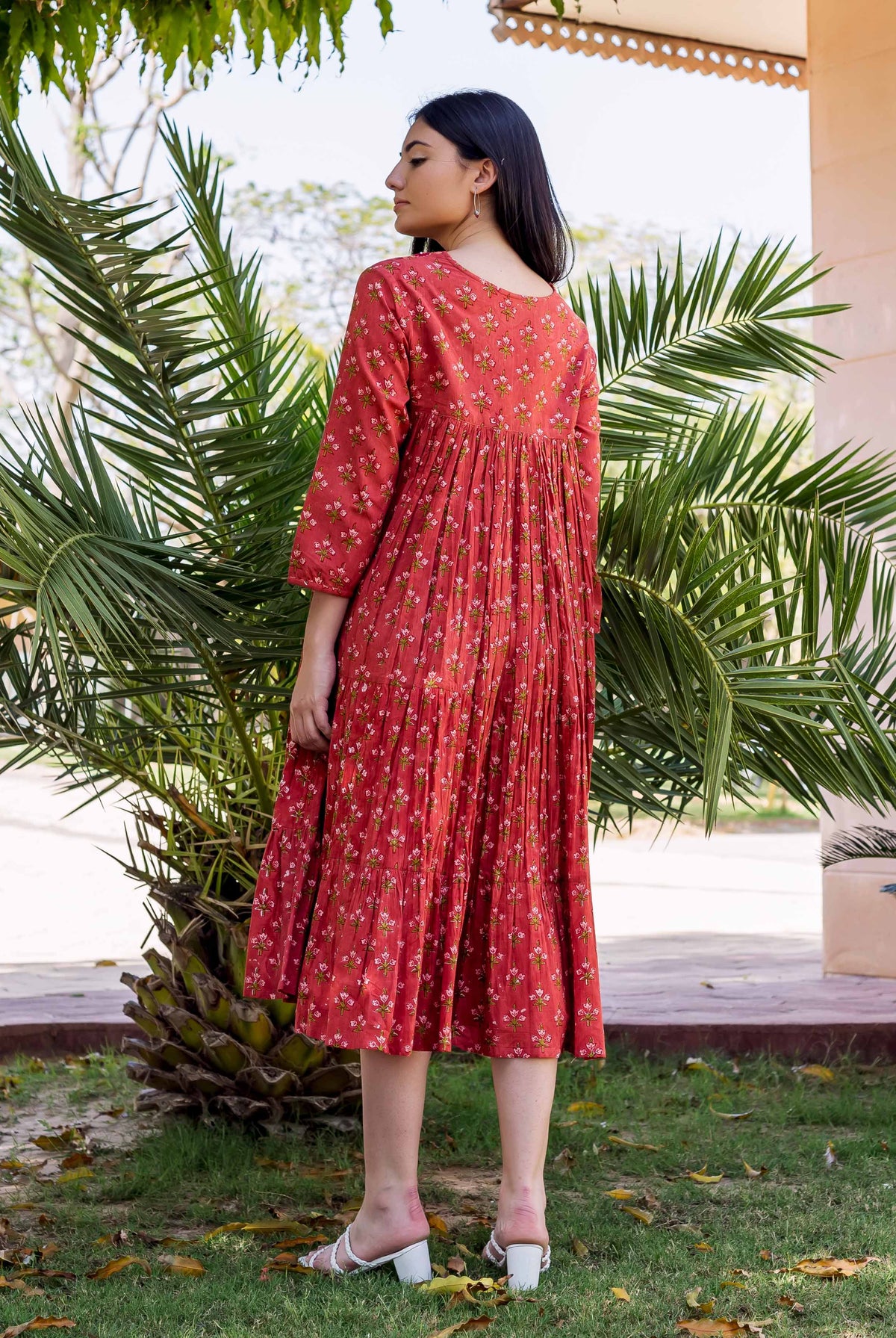 Model wearing a rust-red hand-block-printed tiered dress with small pink floral pattern.