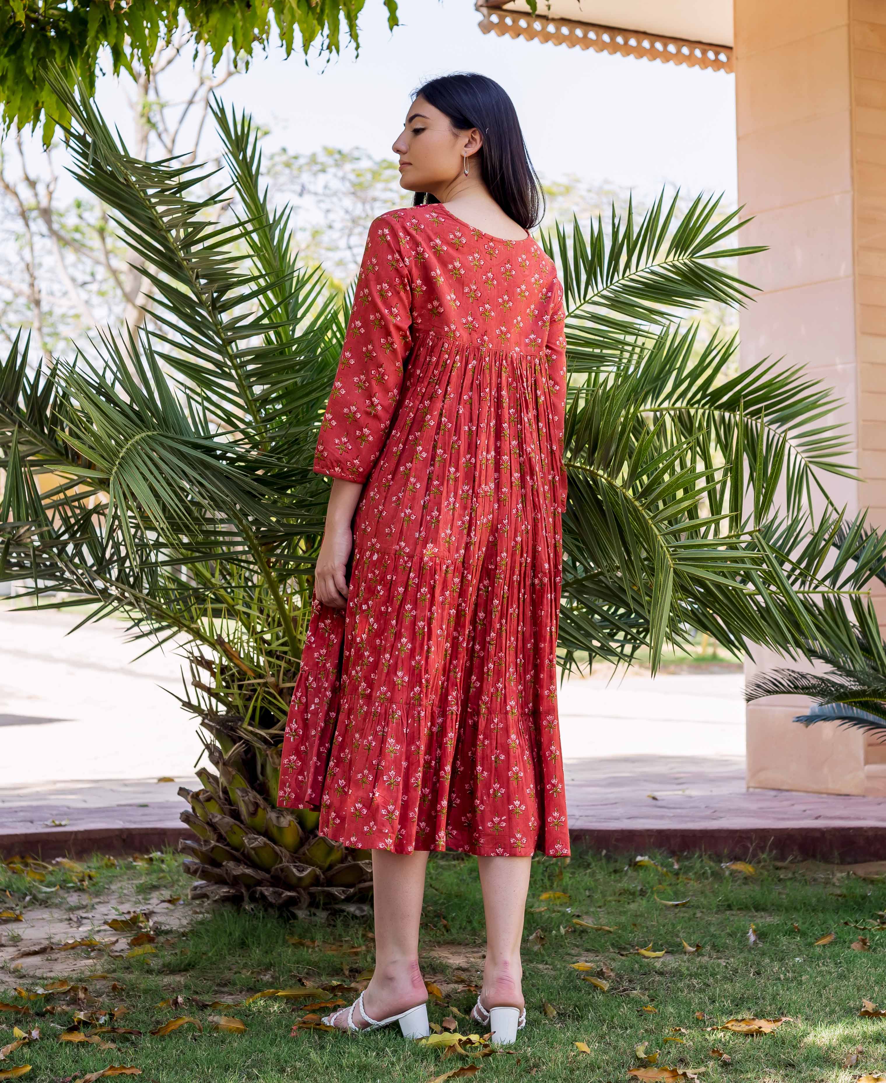 Model wearing a rust-red hand-block-printed tiered dress with small pink floral pattern.