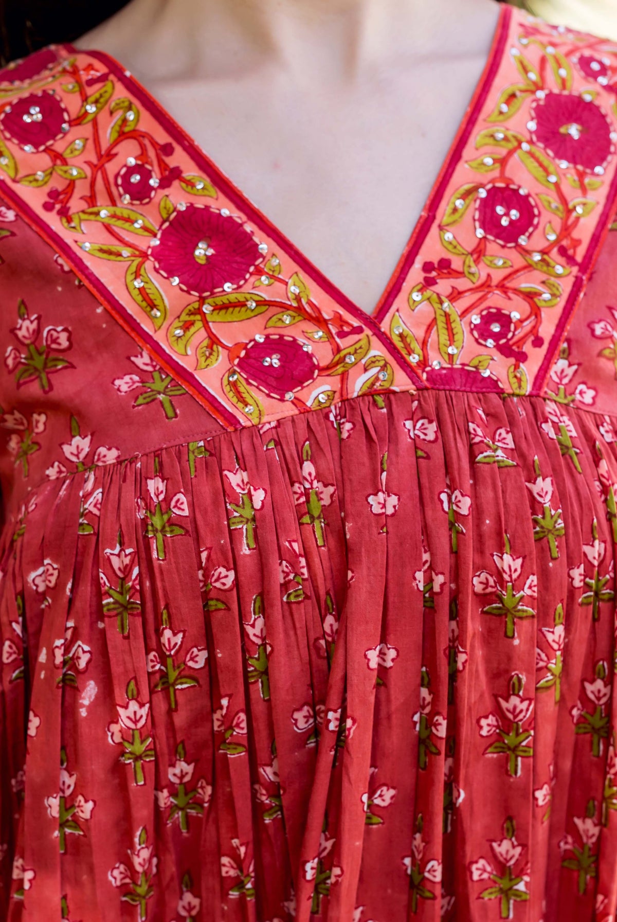 Front close-up of model in red hand-block printed floral tiered dress with embellished V-neck.