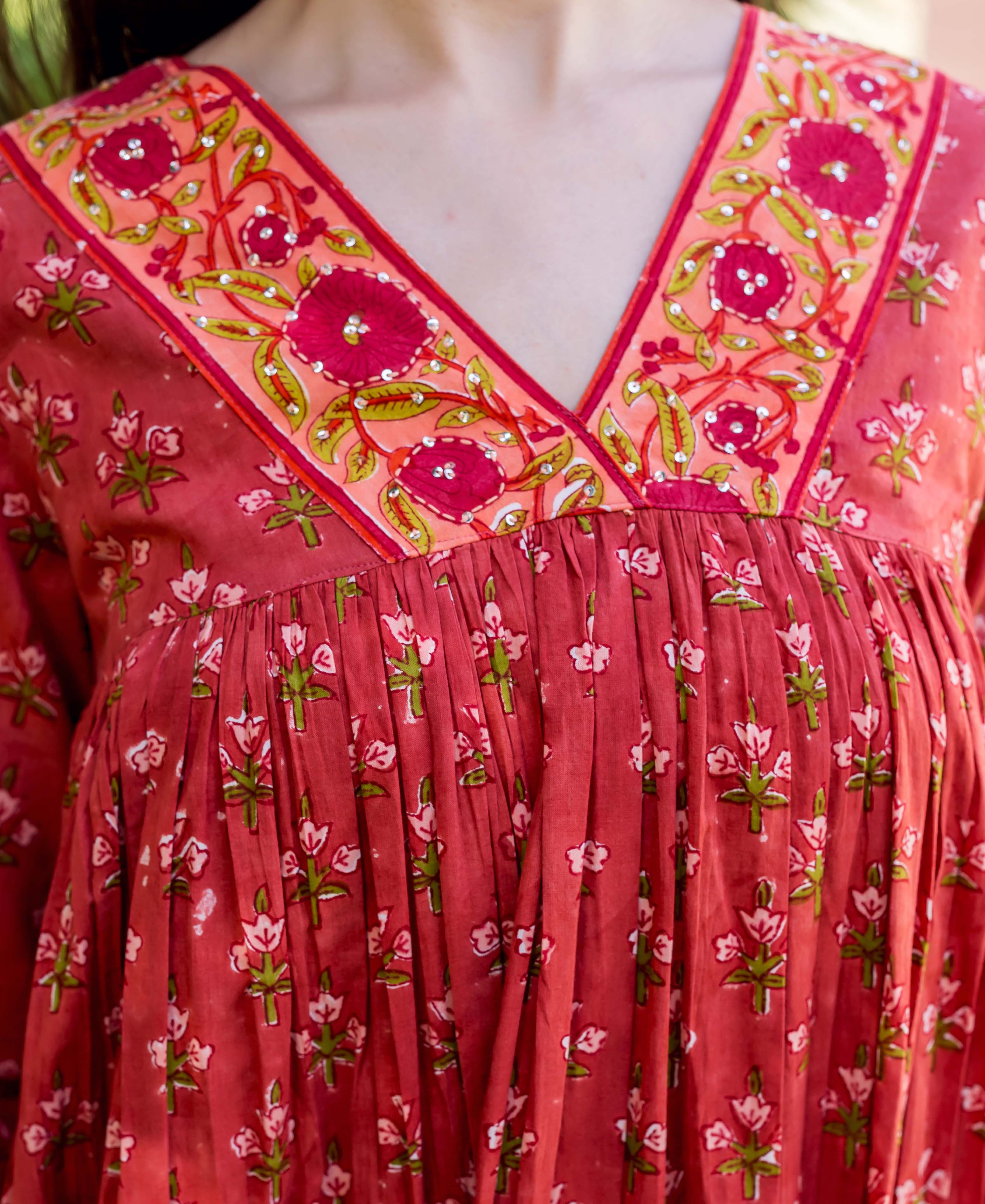 Front close-up of model in red hand-block printed floral tiered dress with embellished V-neck.