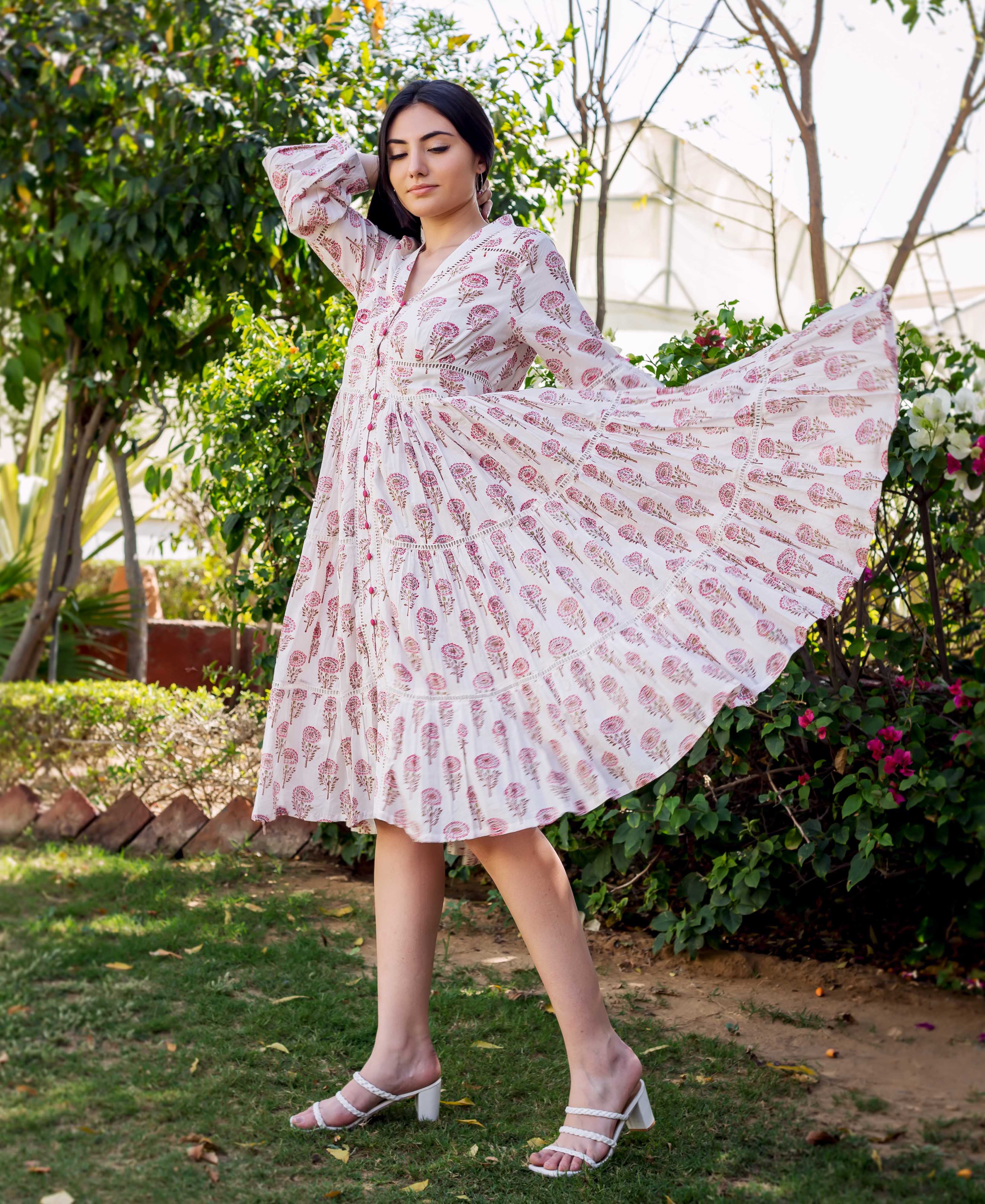 Woman in a flowing white and pink block printed tiered dress with lace trim.