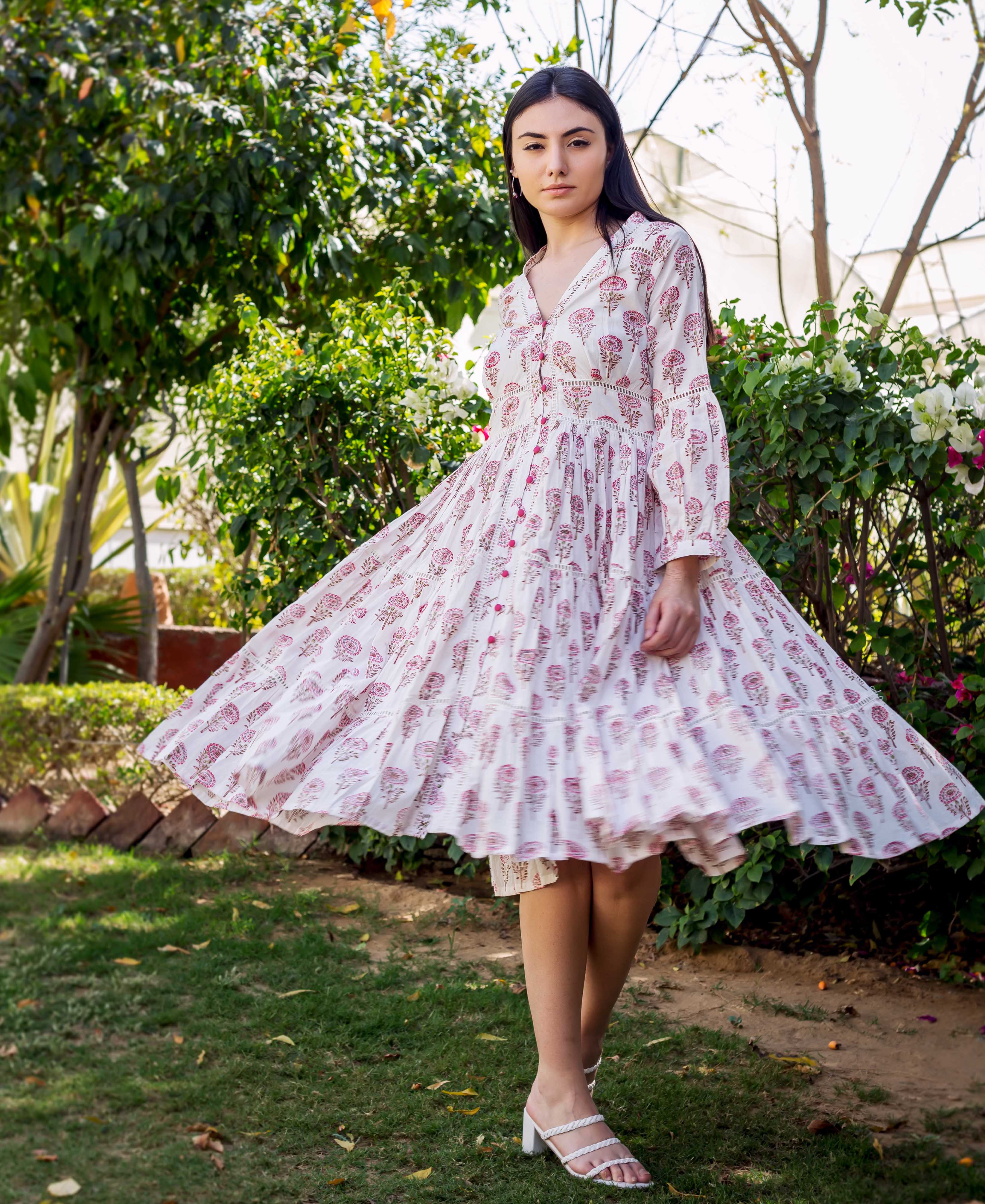 Model twirling in a white and pink block-printed tiered dress with lace details.