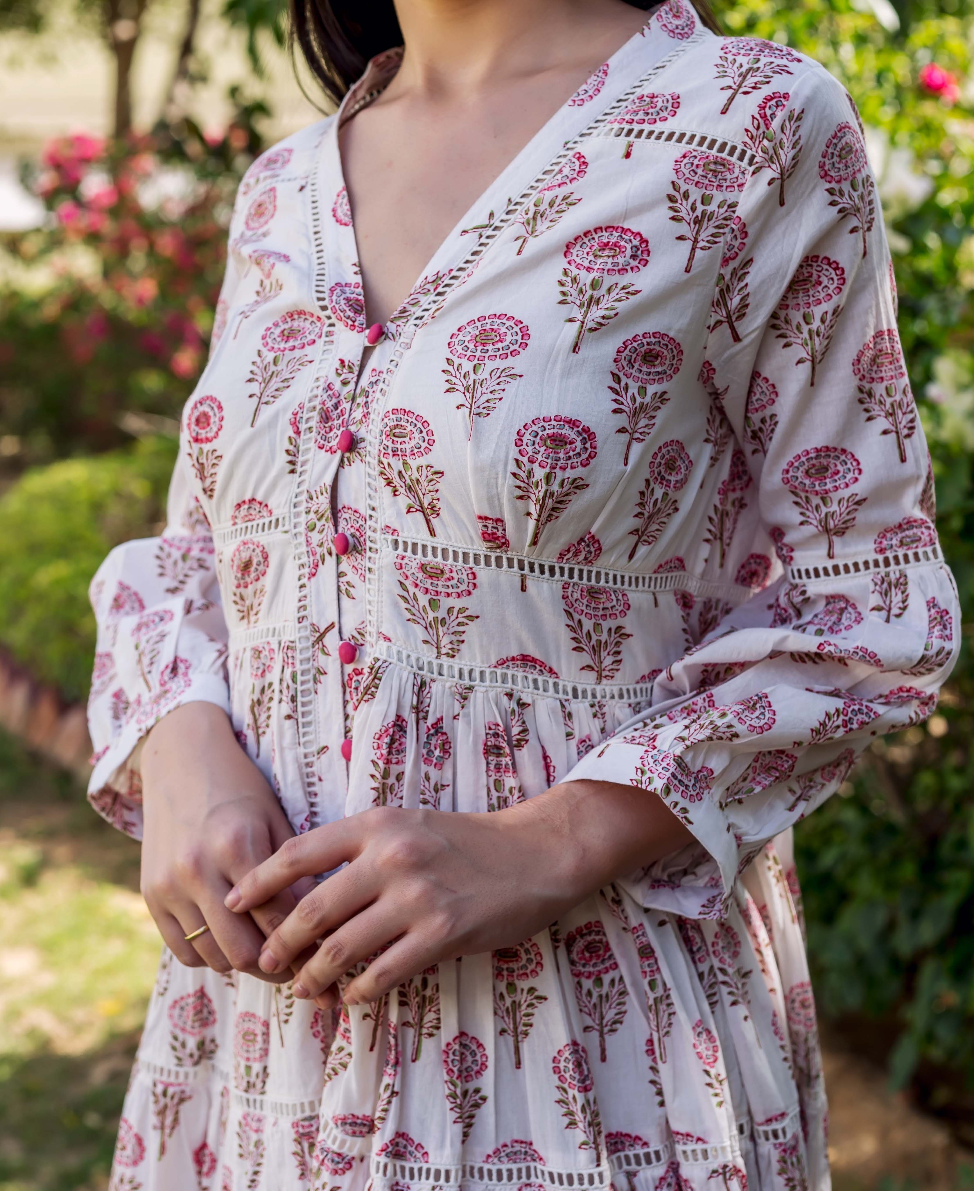 Mid-shot of model wearing white tiered dress with pink block print, lace, and buttons.