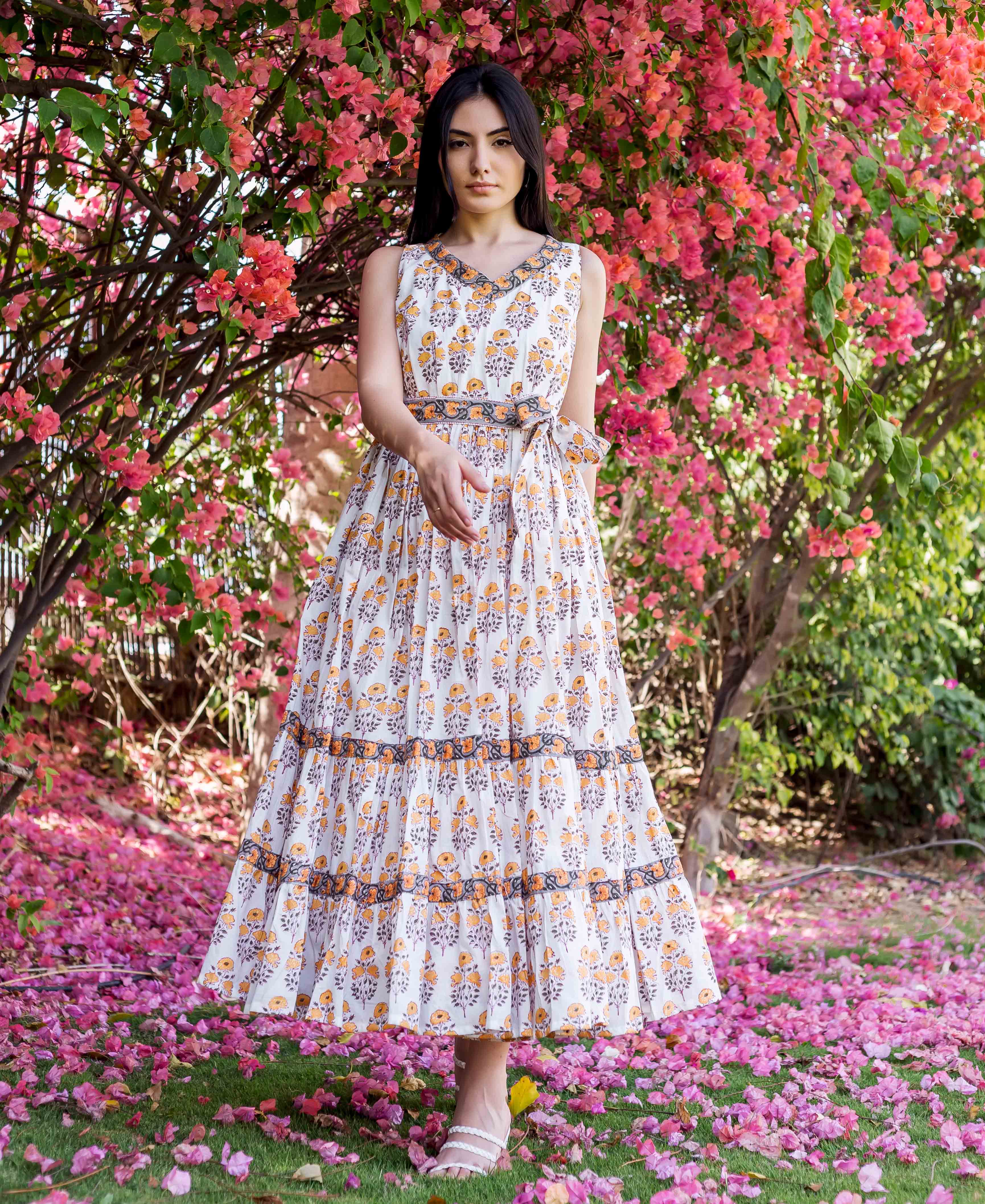 Standing model in white and yellow block-printed floral tiered dress with dark trim.