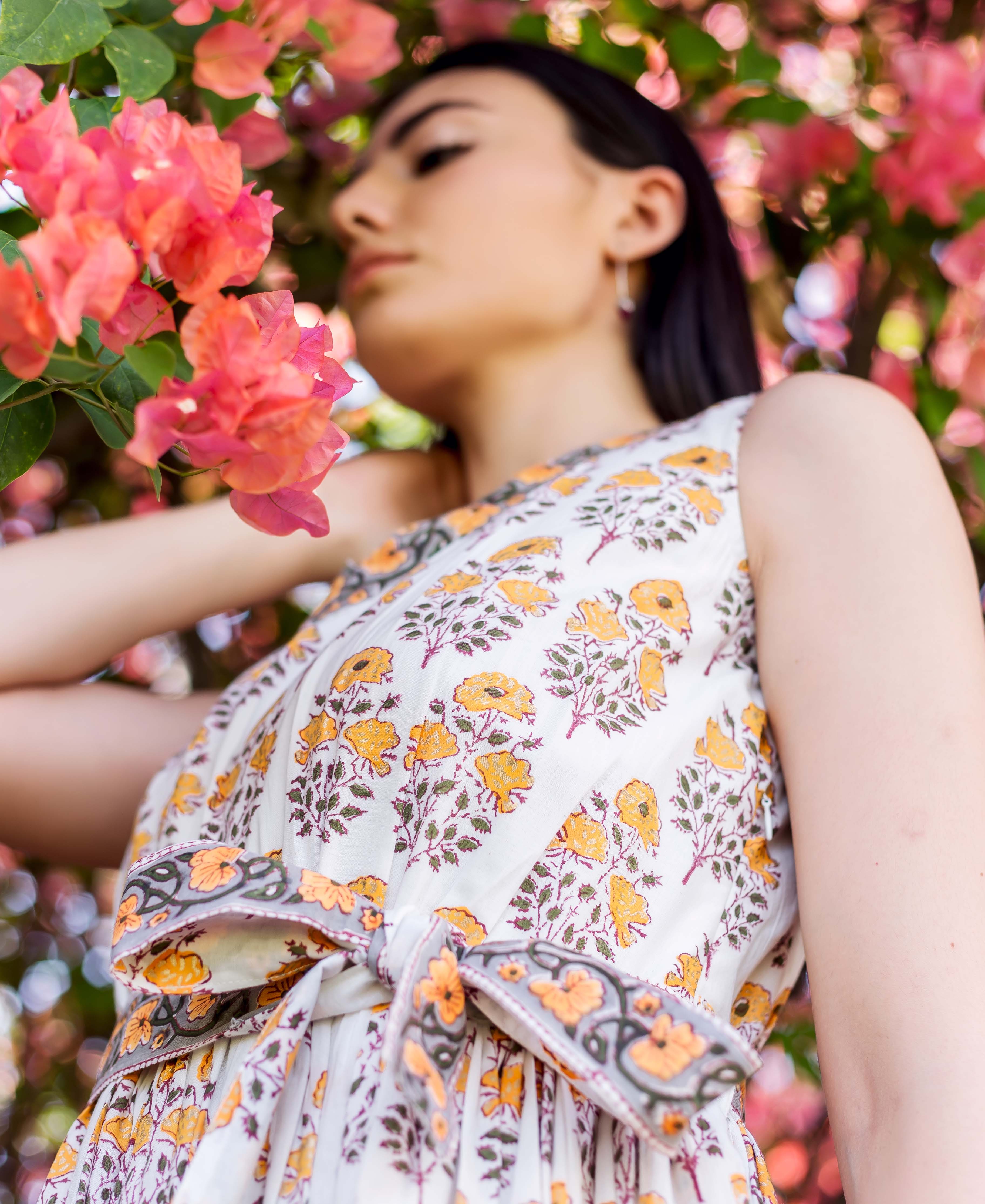 Model in a white block printed dress with yellow floral design and a knotted waist tie.