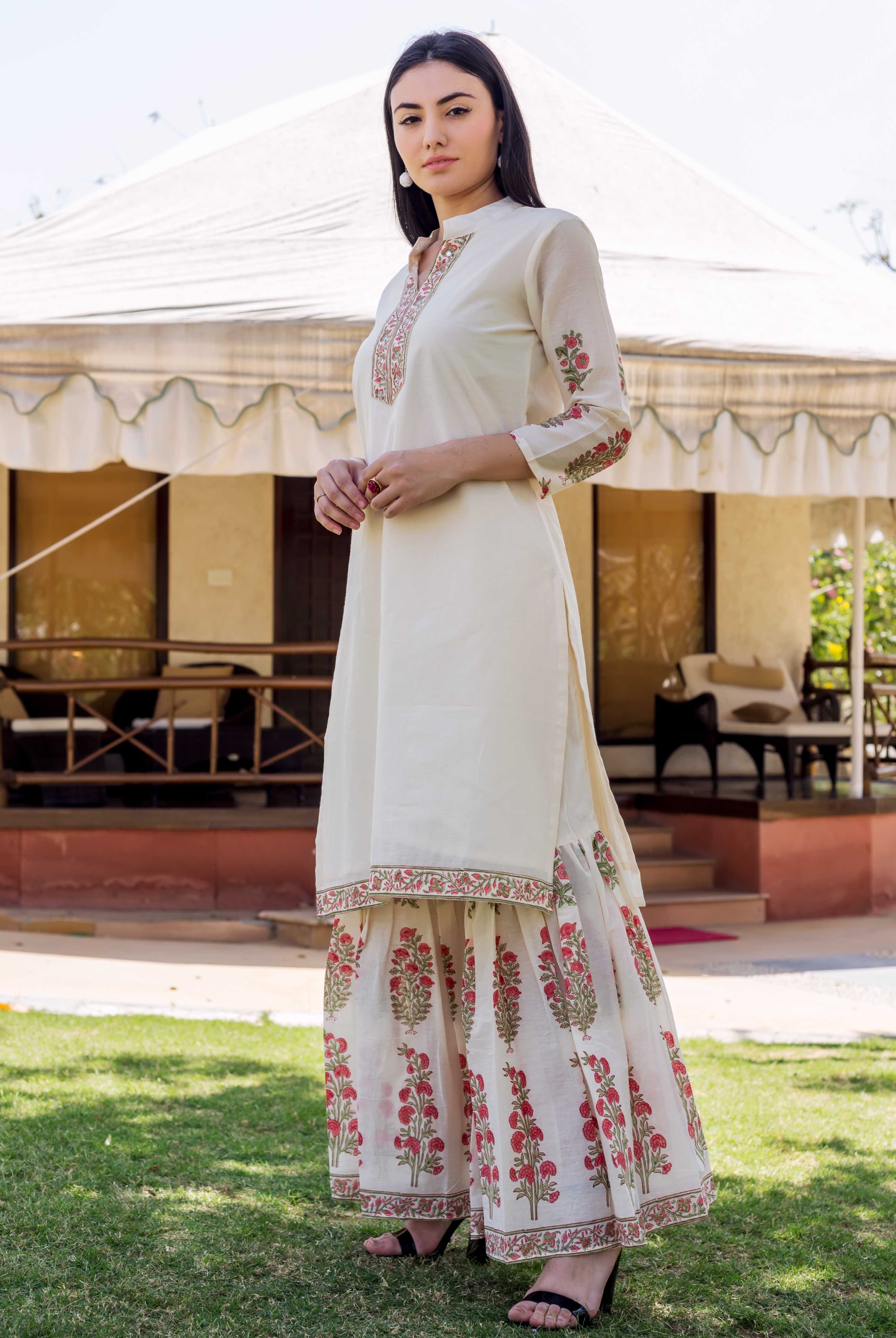 A woman in a long, white kurta with red and green floral prints.