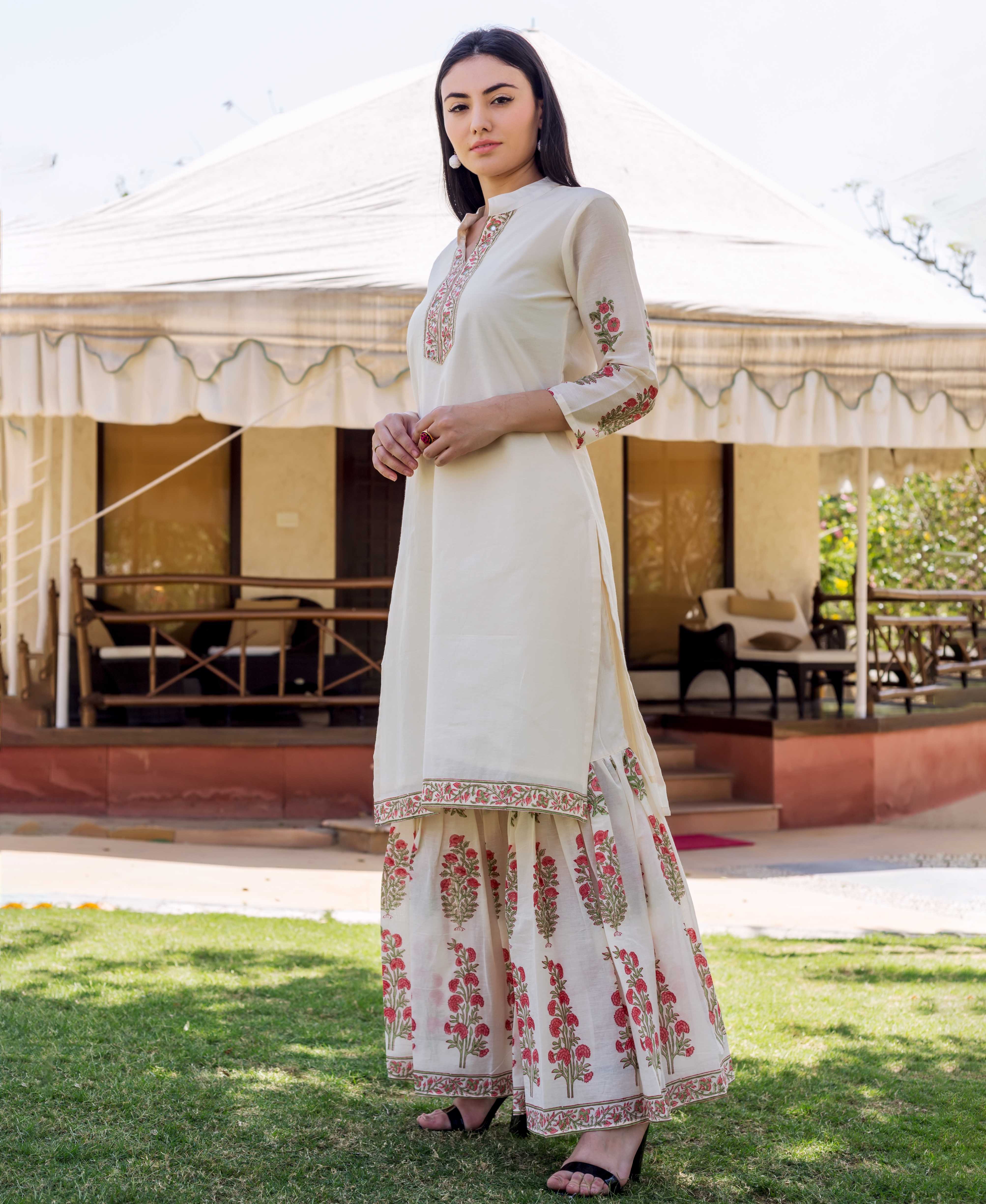 A woman in a long, white kurta with red and green floral prints.