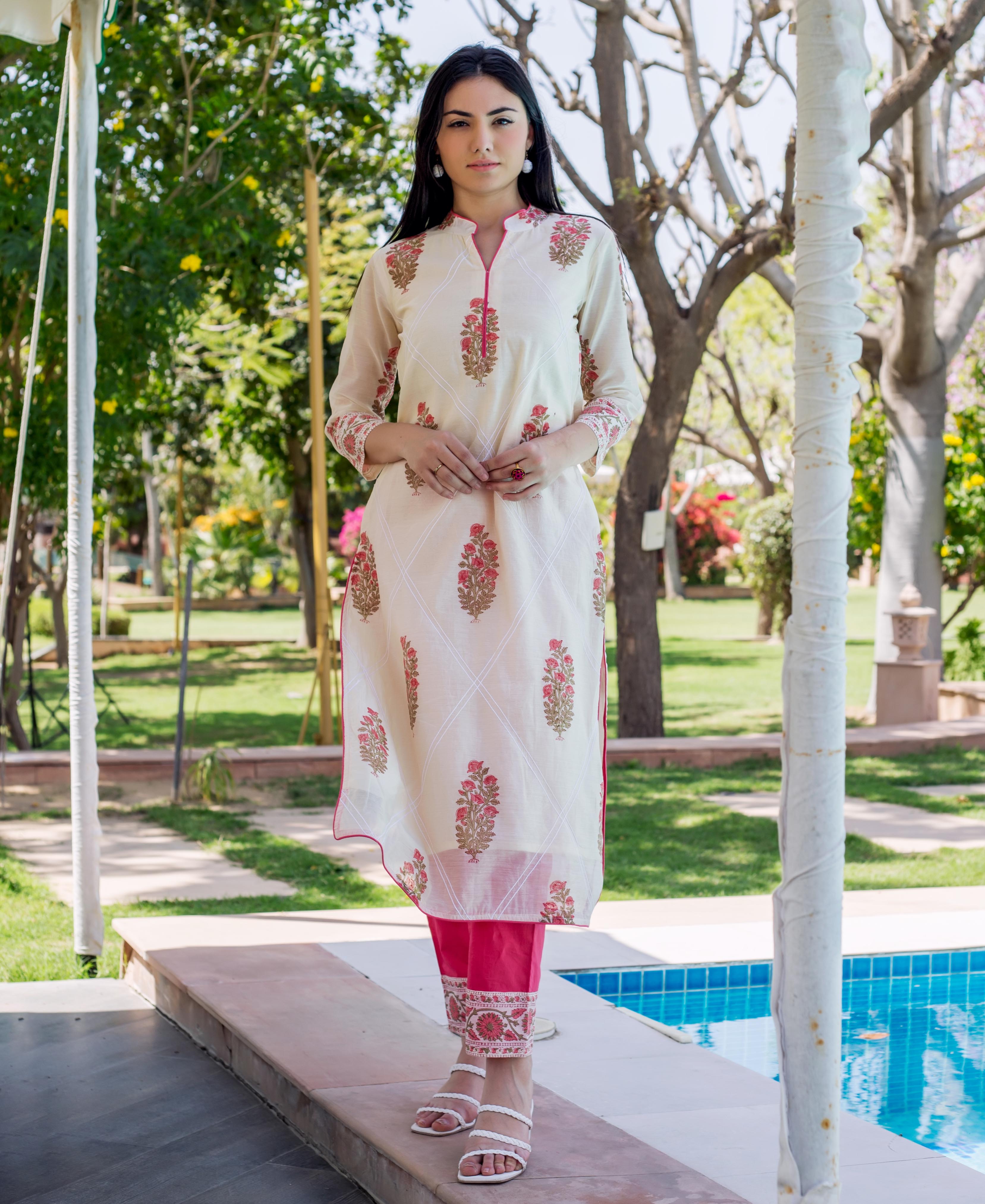 Woman wears off-white straight kurta with pink and gold floral print, pink trim and trousers.