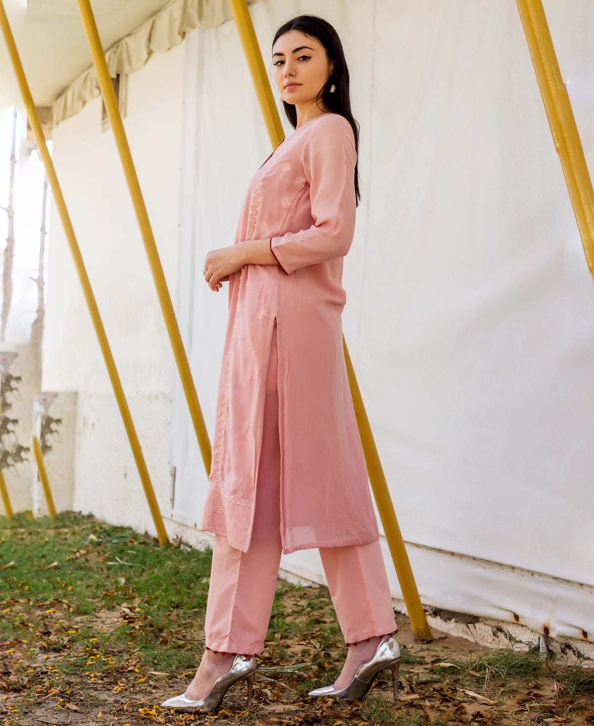 A woman in a dusty pink embroidered kurta and pants, standing outdoors.