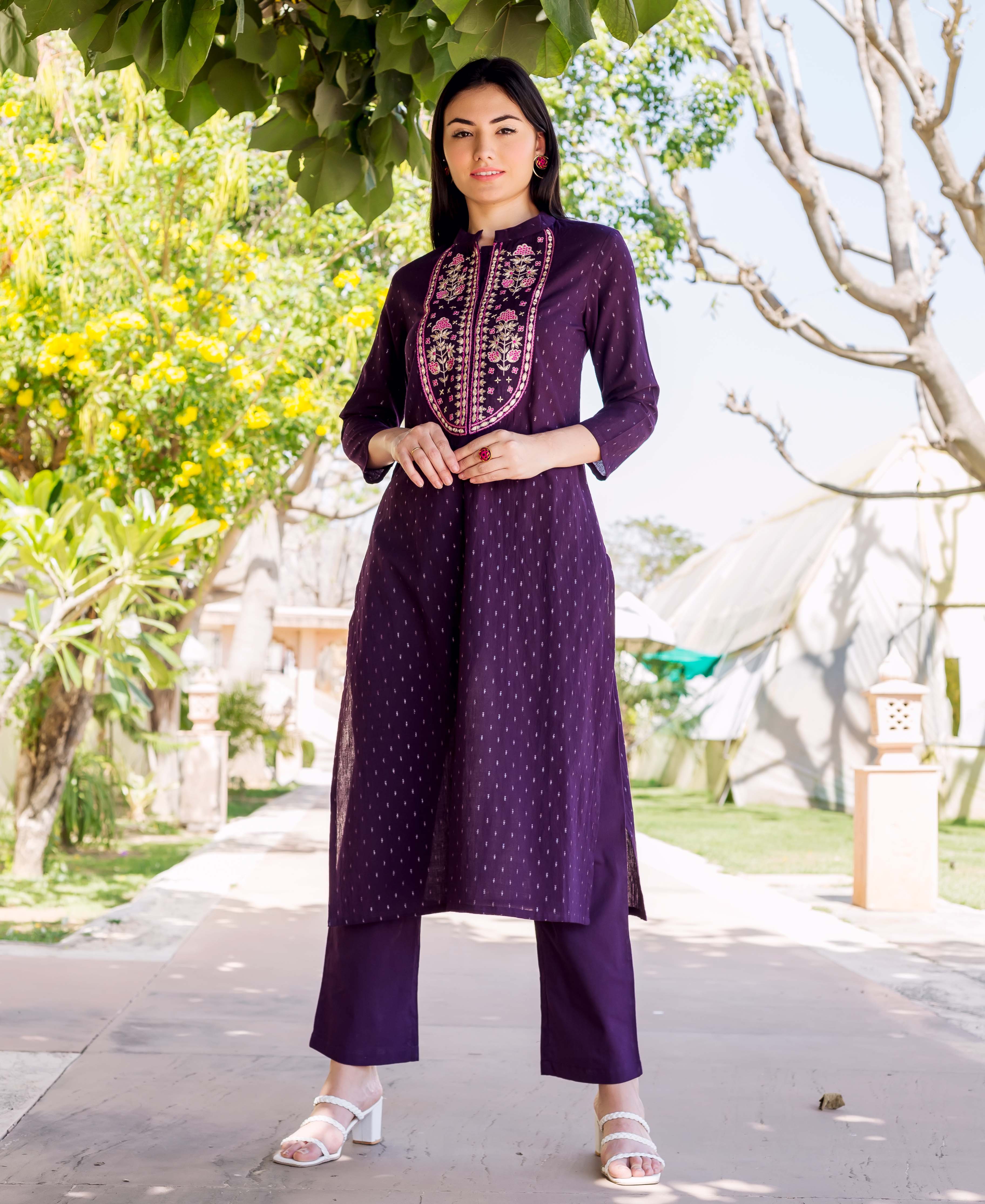 Full-length model wears deep purple Lurex kurta with pink floral embroidered neckline and matching pants.
