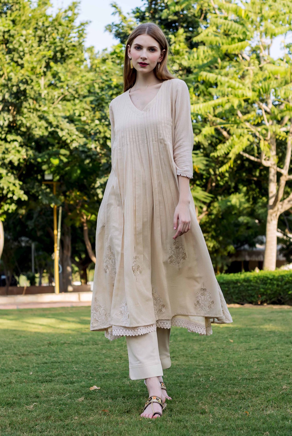 Model in full shot wearing a beige embroidered kurta with lace trim, walking outdoors.