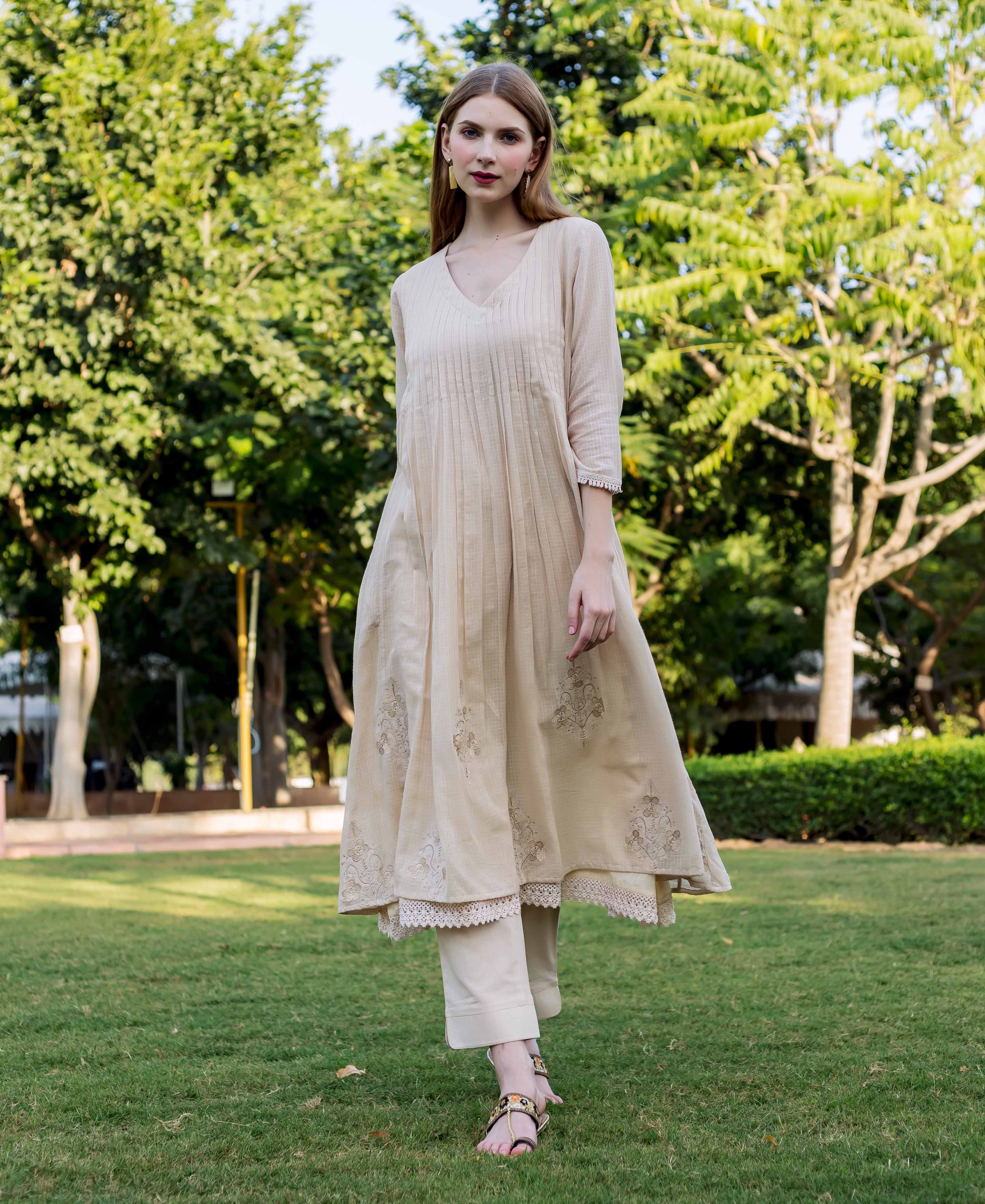 Model in full shot wearing a beige embroidered kurta with lace trim, walking outdoors.