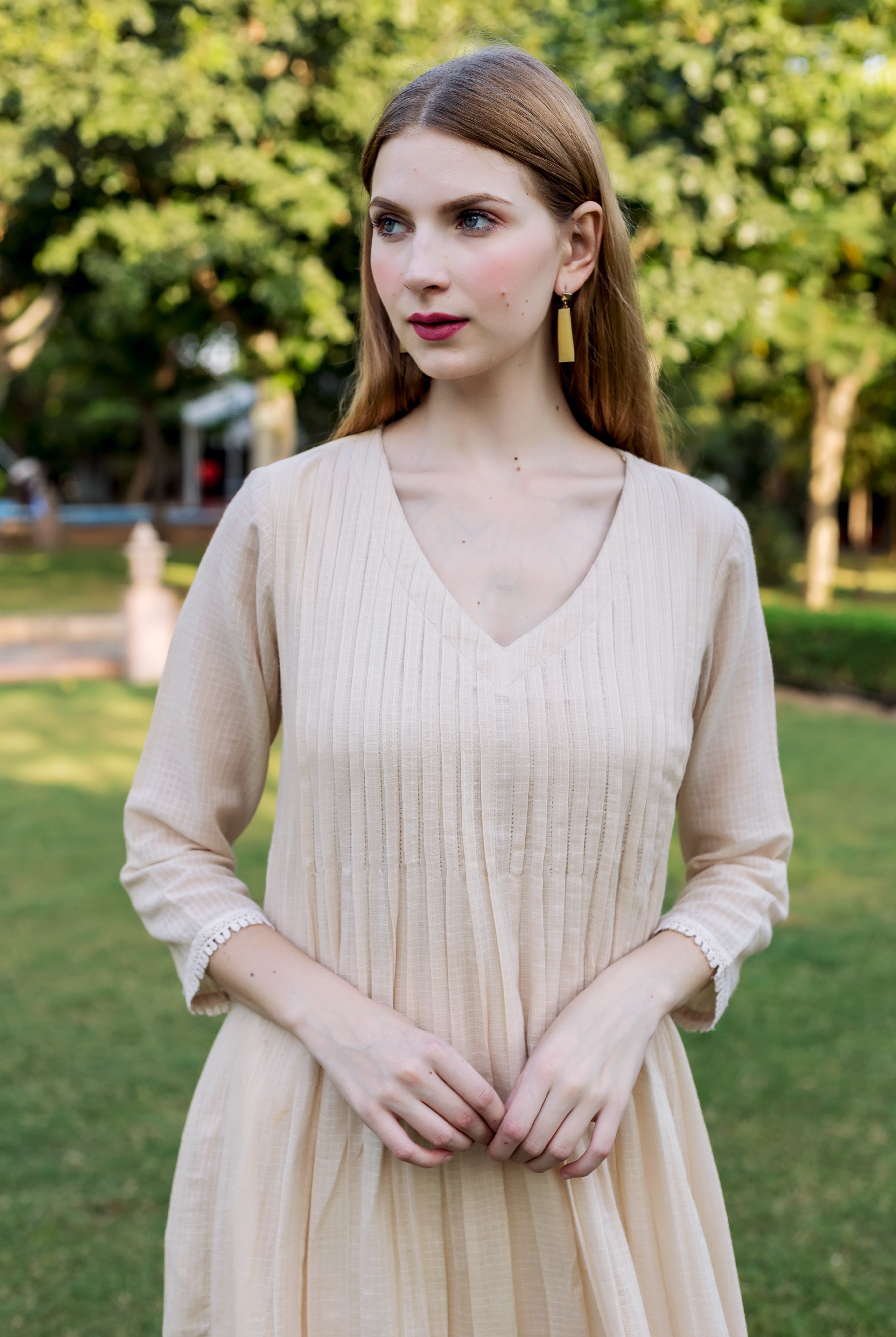 Woman wearing a beige V-neck kurta with pintucked bodice, textured fabric, and lace trim.