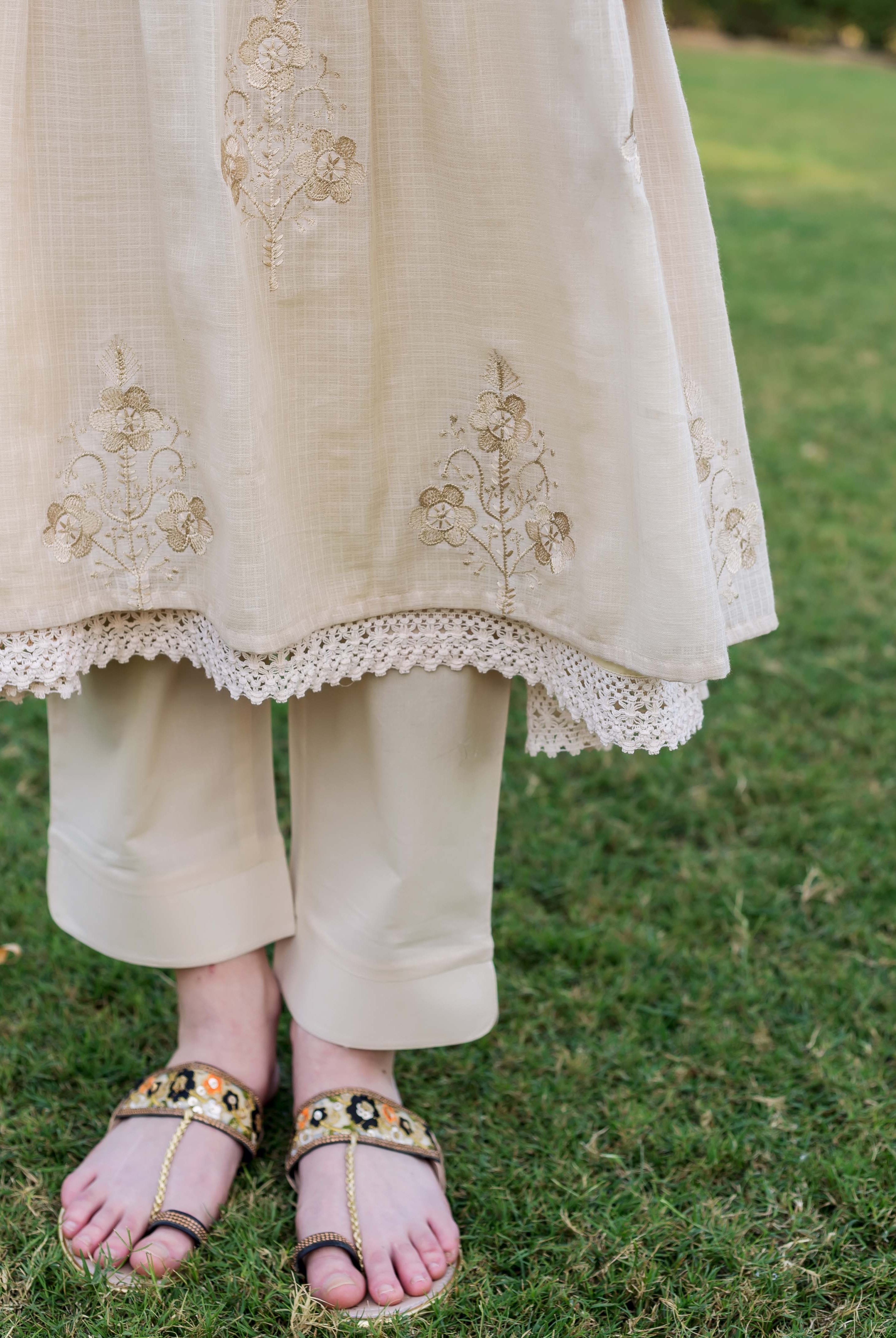 Lower body of model in beige embroidered kurta, lace trim, matching trousers, and ornate sandals.