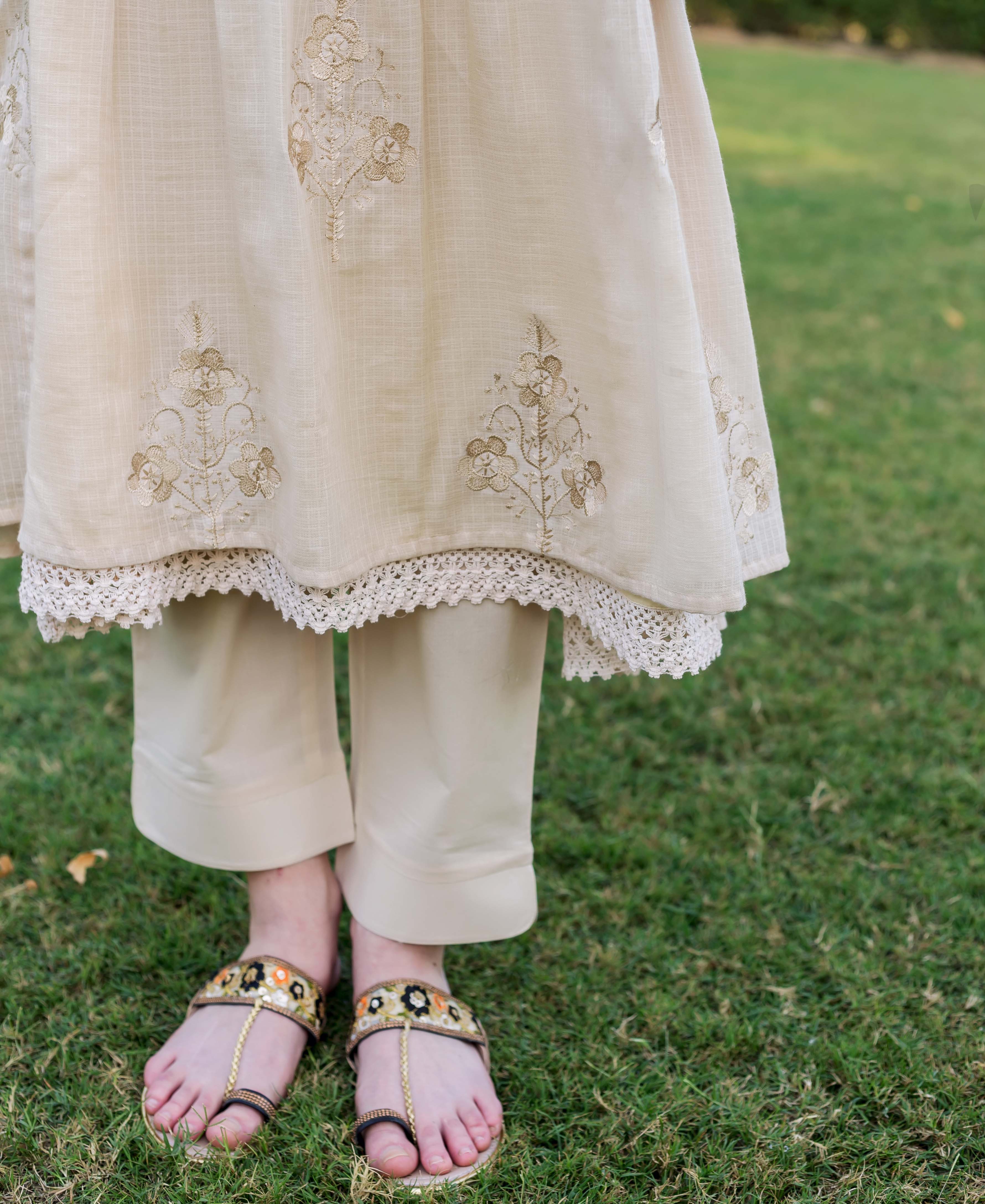 Lower body of model in beige embroidered kurta, lace trim, matching trousers, and ornate sandals.