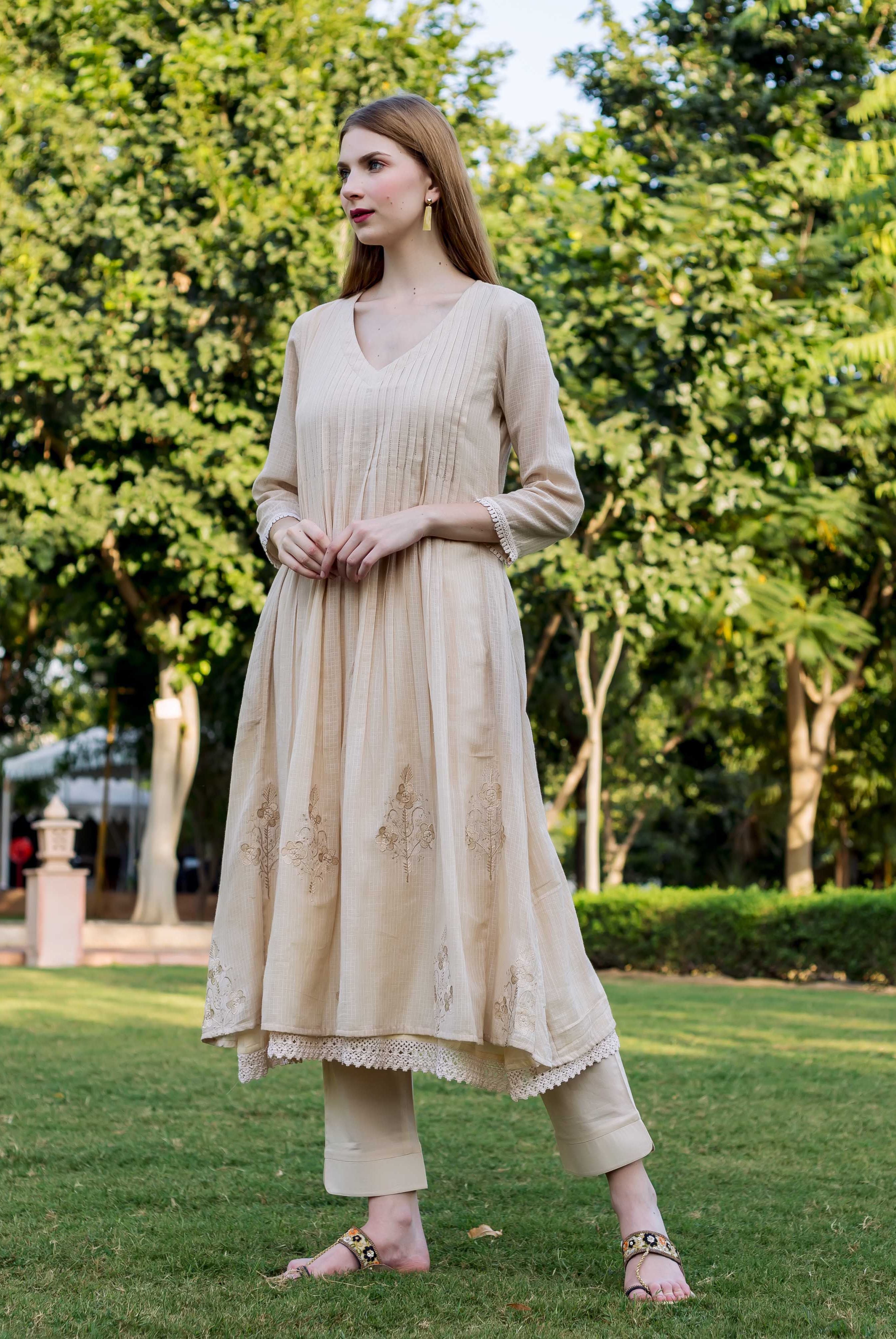 Model in a full-length beige kurta featuring pintucks, intricate embroidery, and lace trim.