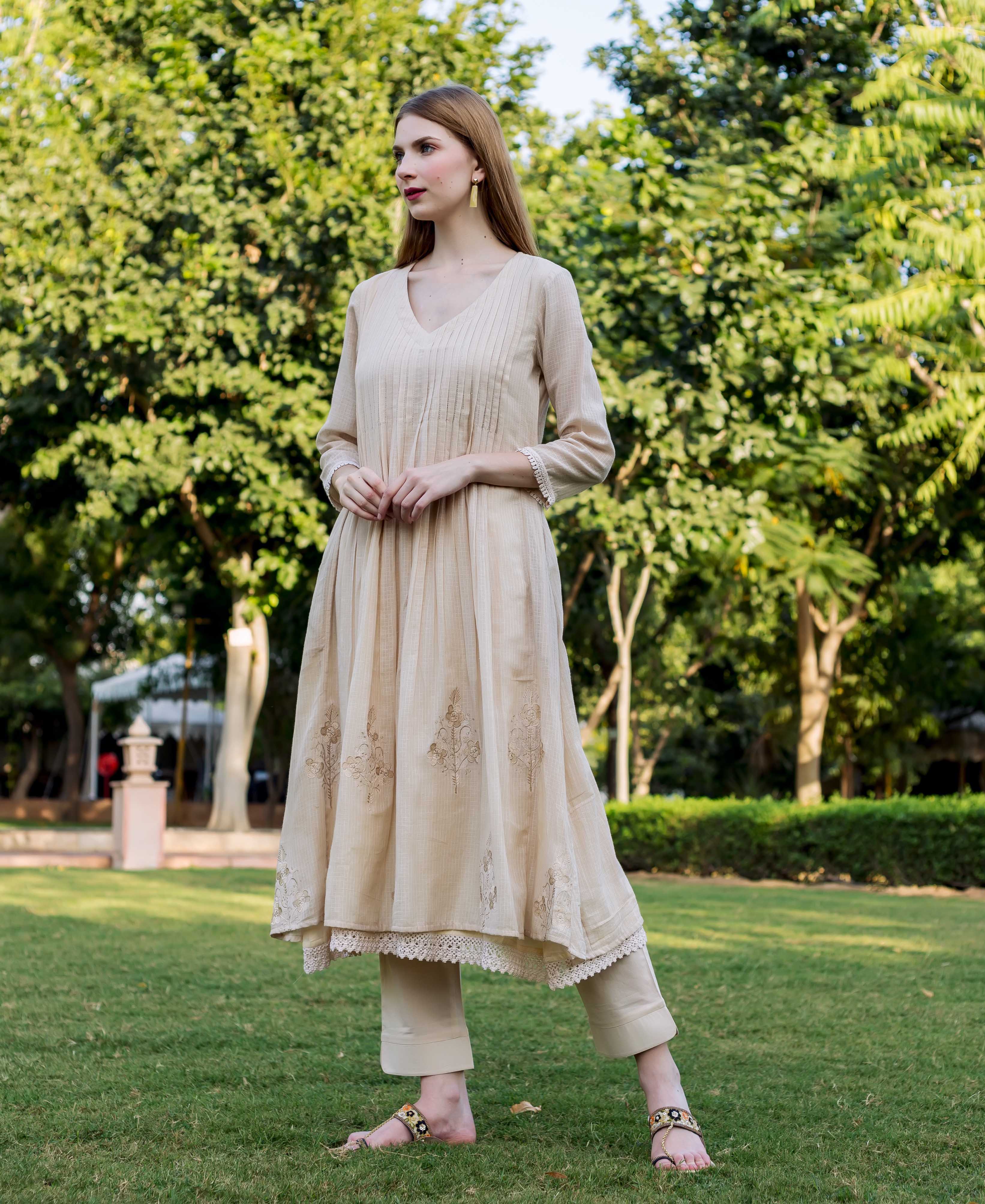 Model in a full-length beige kurta featuring pintucks, intricate embroidery, and lace trim.